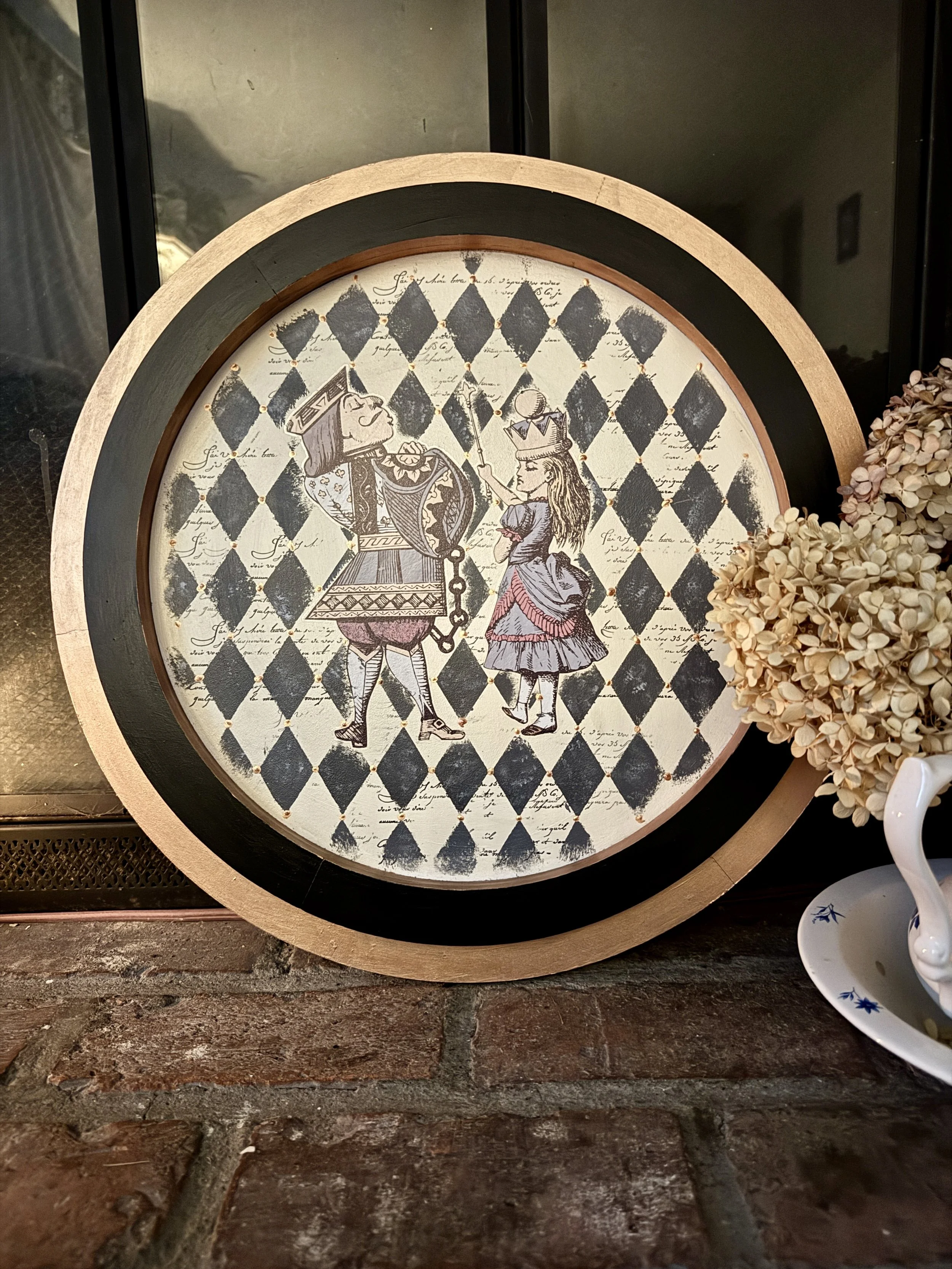 Decorative round wall art featuring a medieval-style illustration of a king and a princess against a background of black and white diamond pattern with handwritten script.