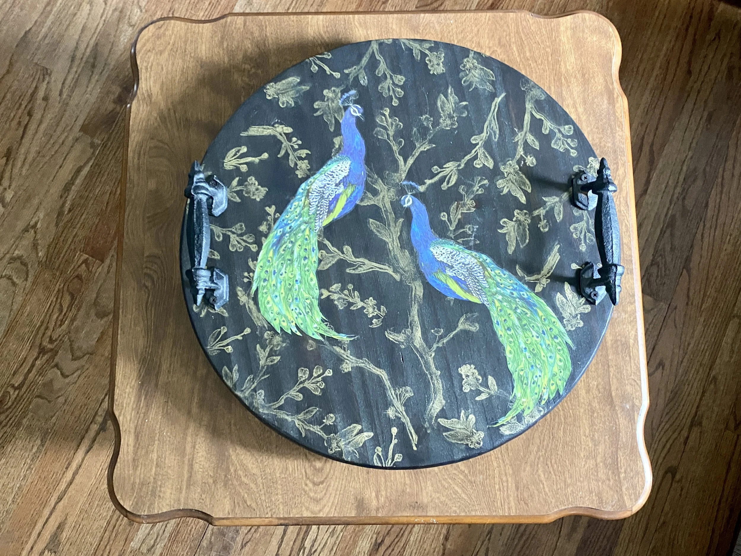 Decorative tray with a painted peacock and gold leaf pattern, placed on a wooden table.