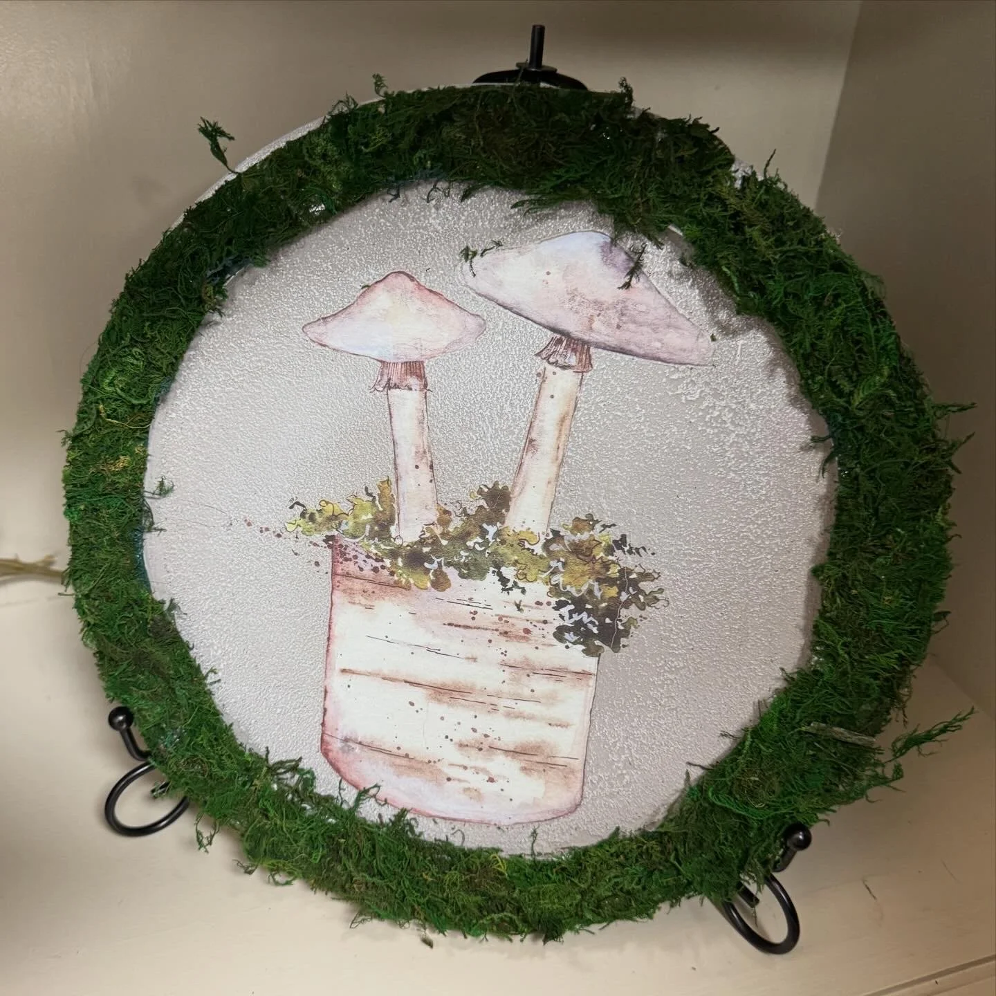 Decorative tabletop with a painted image of two mushrooms in a flower pot, surrounded by a green moss border.