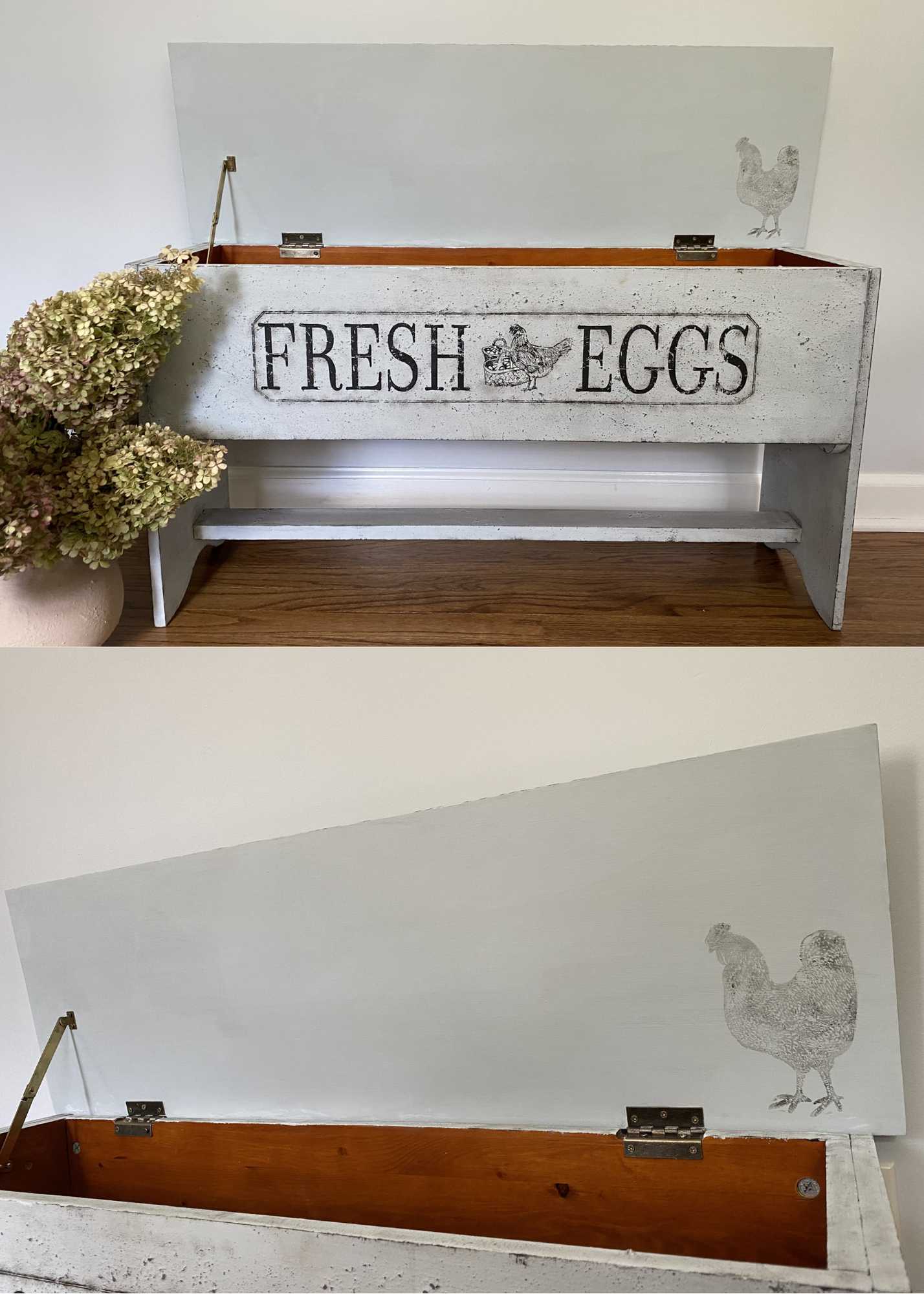 A white wooden chicken coop with a hinged lid that is open, showing an interior with a wooden bottom. The front of the coop has black stencil lettering that says 'FRESH EGGS' with a chicken illustration between the words. To the left of the coop, the