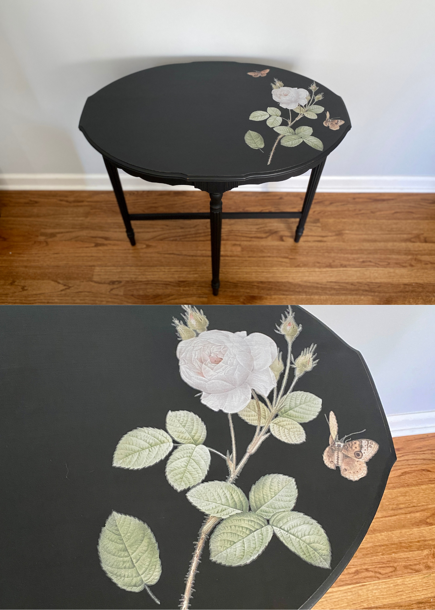 A black, round tabletop decorated with a white rose design surrounded by green leaves and butterflies, with a hardwood floor and a white wall in the background.