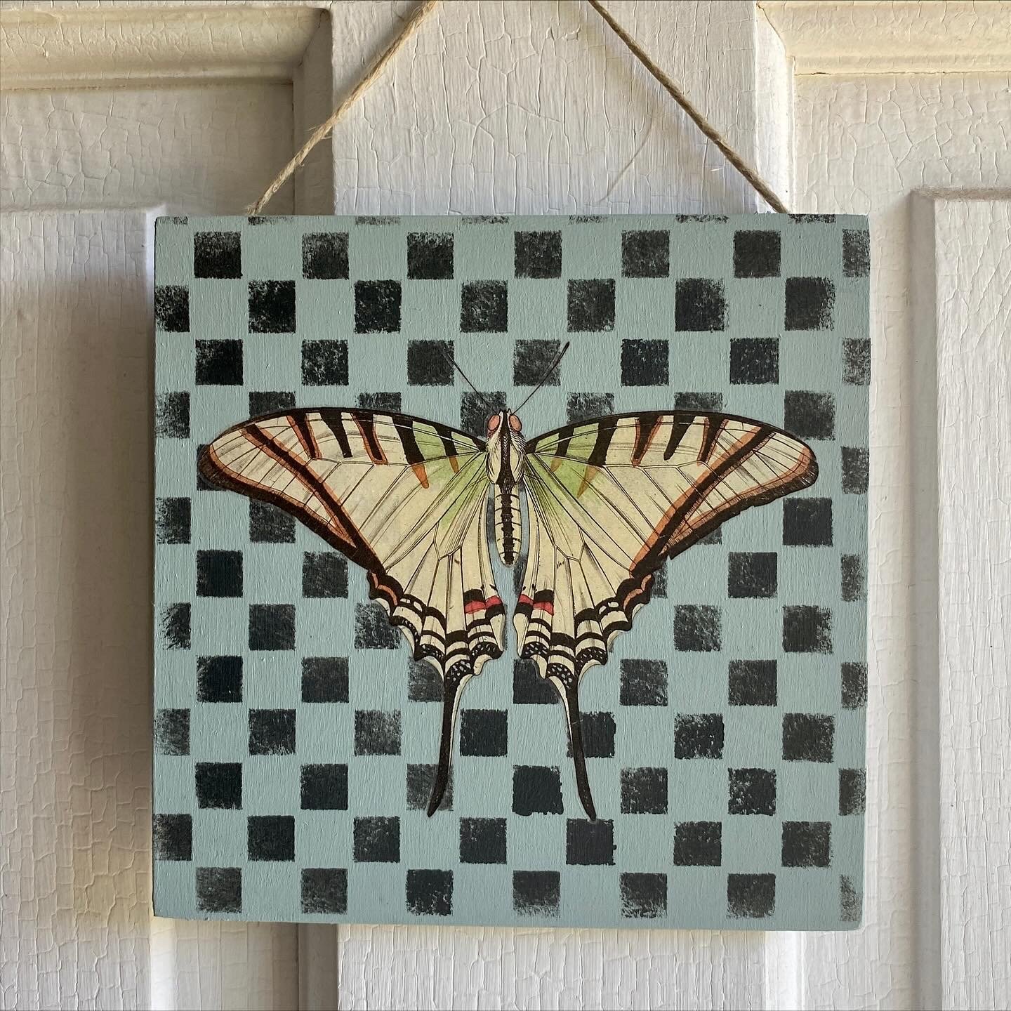 A painting of a butterfly with yellow and black wings on a blue background with black checkered pattern.