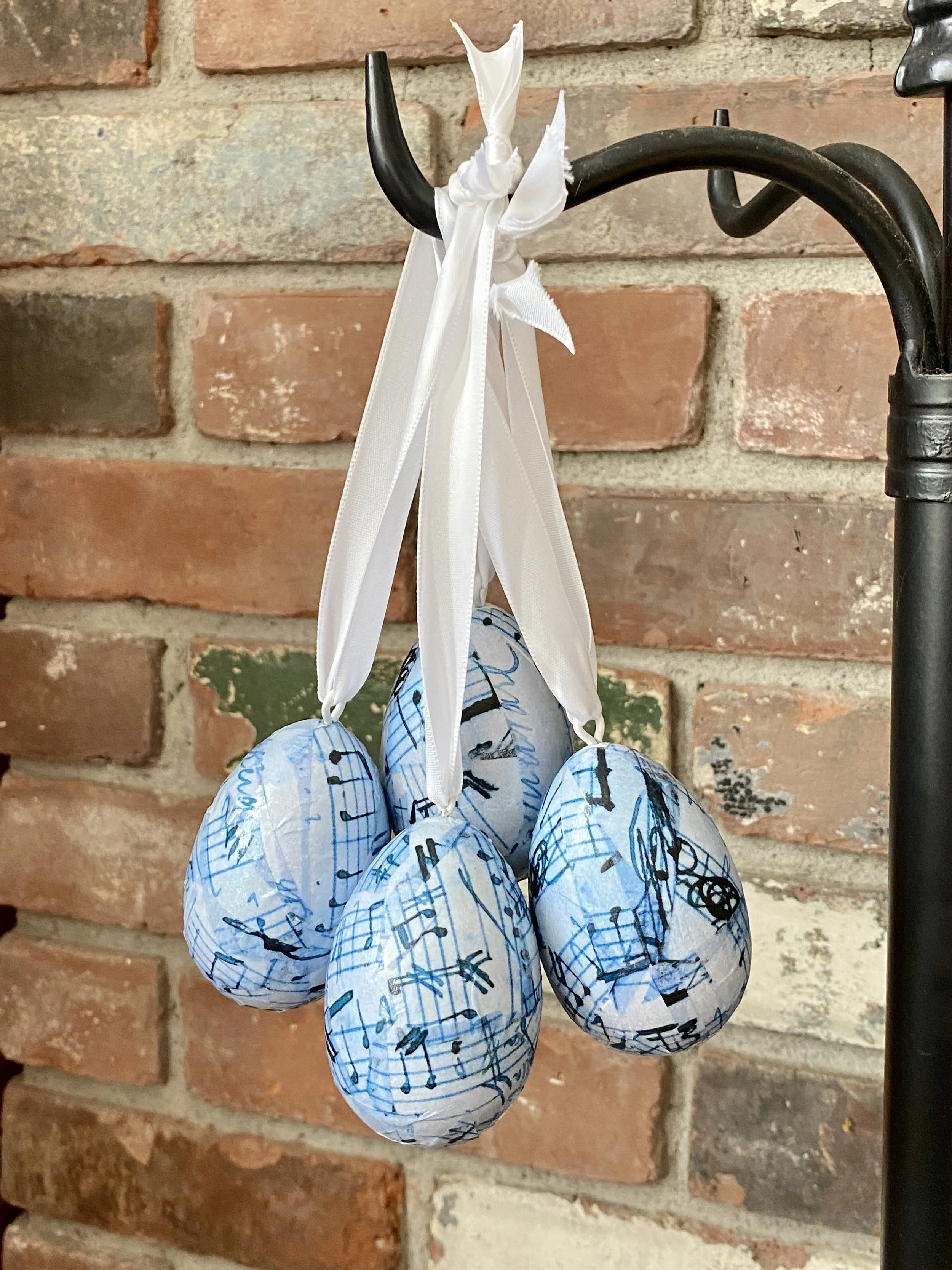 A decorative hanging of small blue paper lanterns with writing on them, tied with white ribbons, against a brick wall background.