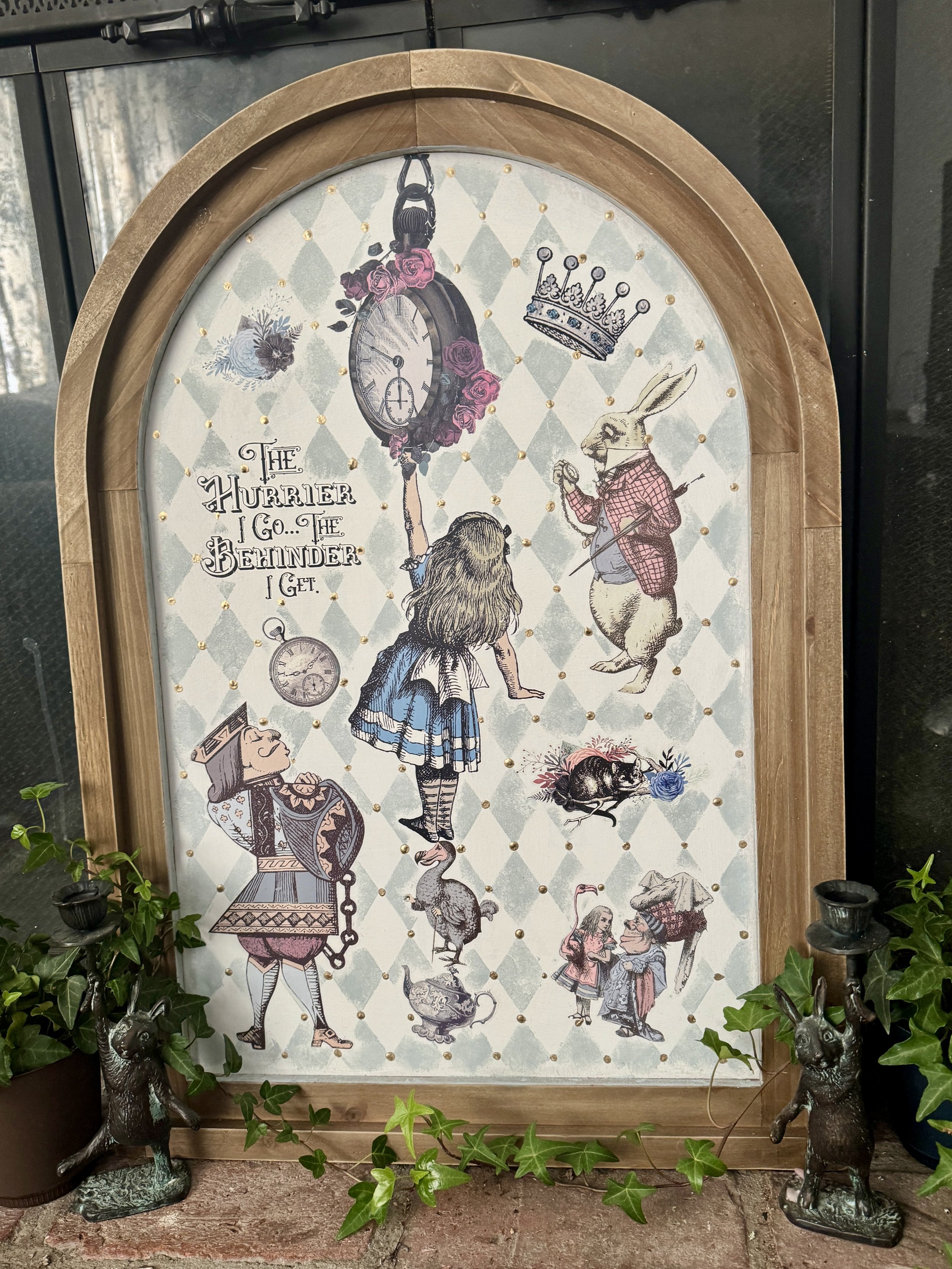 Decorative clock face with illustrations of characters and objects from Alice in Wonderland, including a rabbit, a girl, a cat, a crown, a pocket watch, & a teapot, surrounded by green Ivy plants.