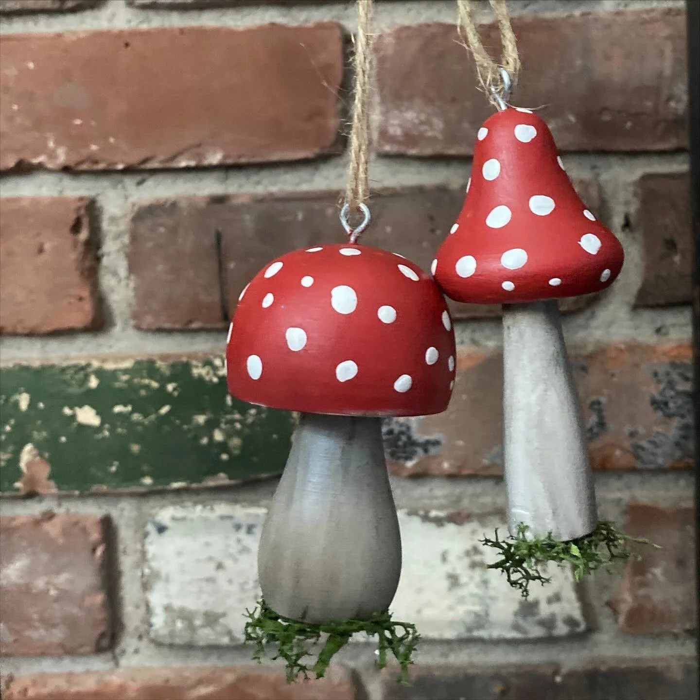 Decorative mushroom ornaments with red caps with white spots and gray stems, hanging in front of a brick wall.