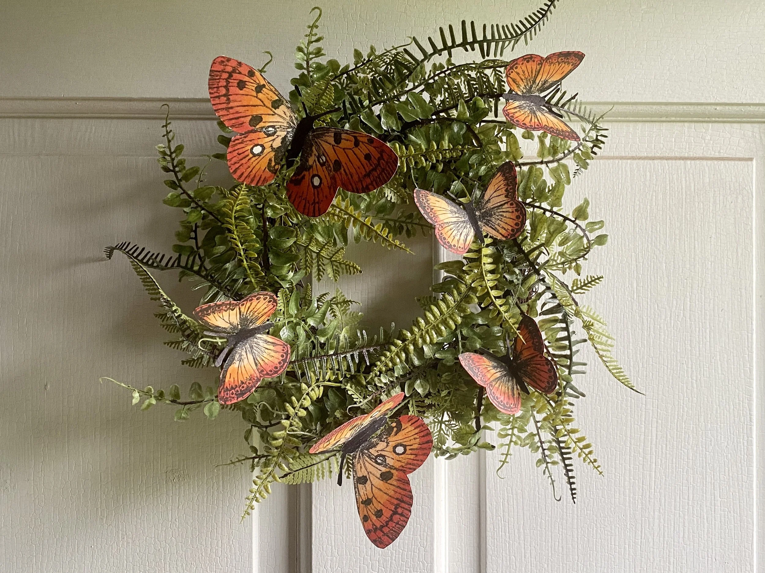 Artificial plant with orange butterflies and green leaves hanging on a wall.