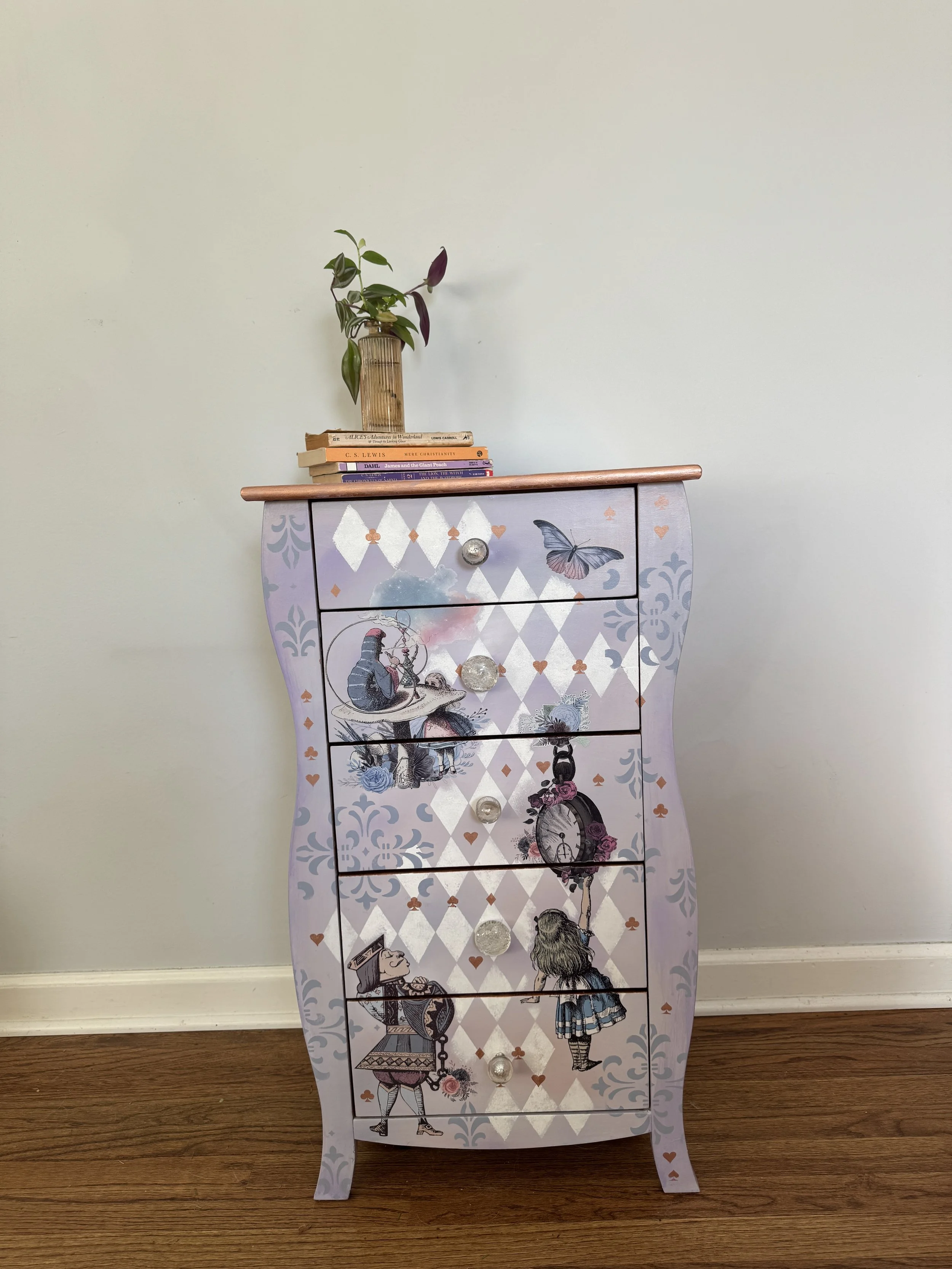 Decorative purple and white dresser with whimsical illustrations, floral and clock motifs, with six drawers and a wooden top. It has a small drawer at the top with a clear knobs, and six larger drawers below with decorative knobs. On top of the dress