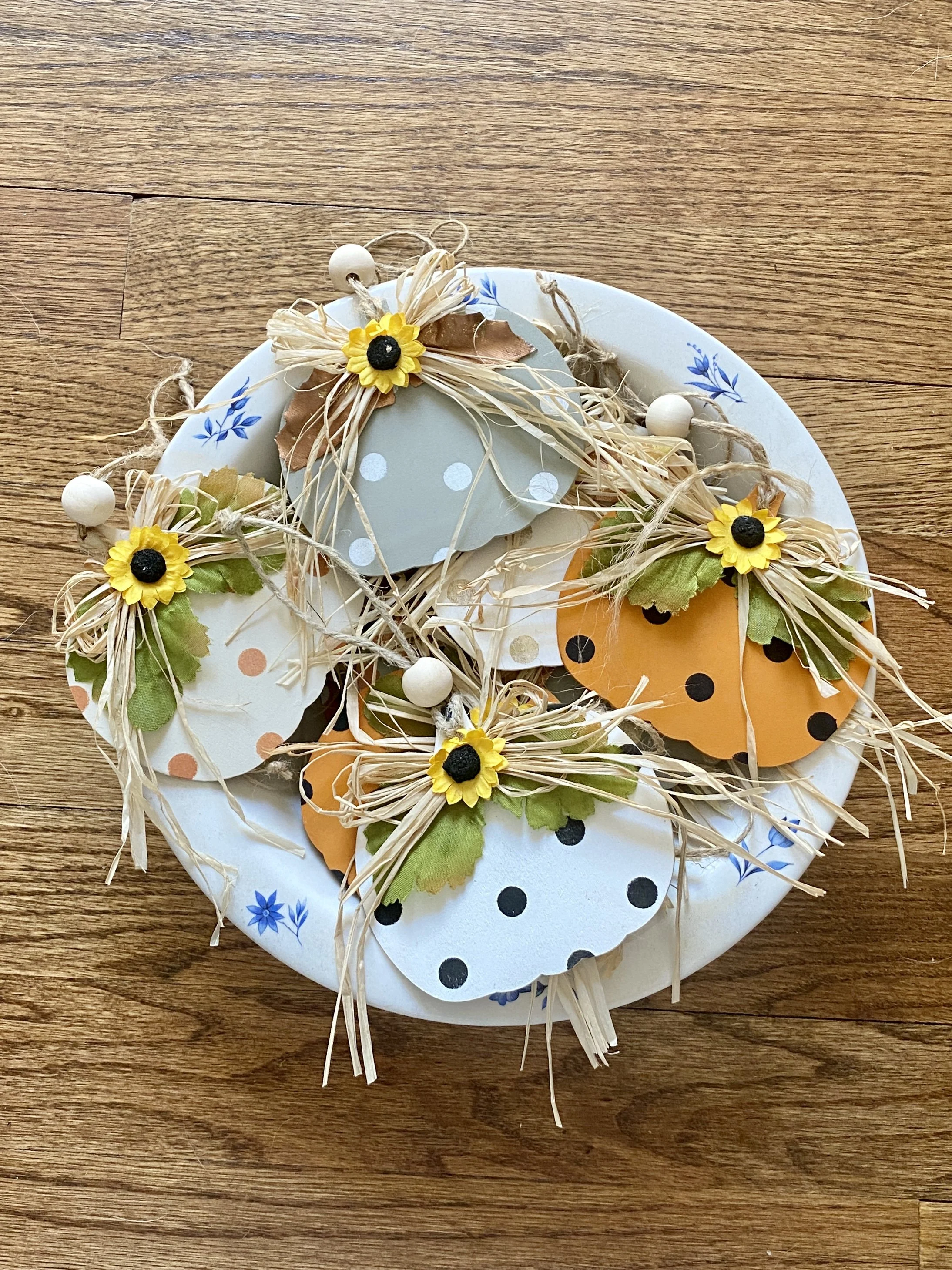 Decorative Easter wreath with paper and artificial flowers, straw, and beads on a wooden surface.