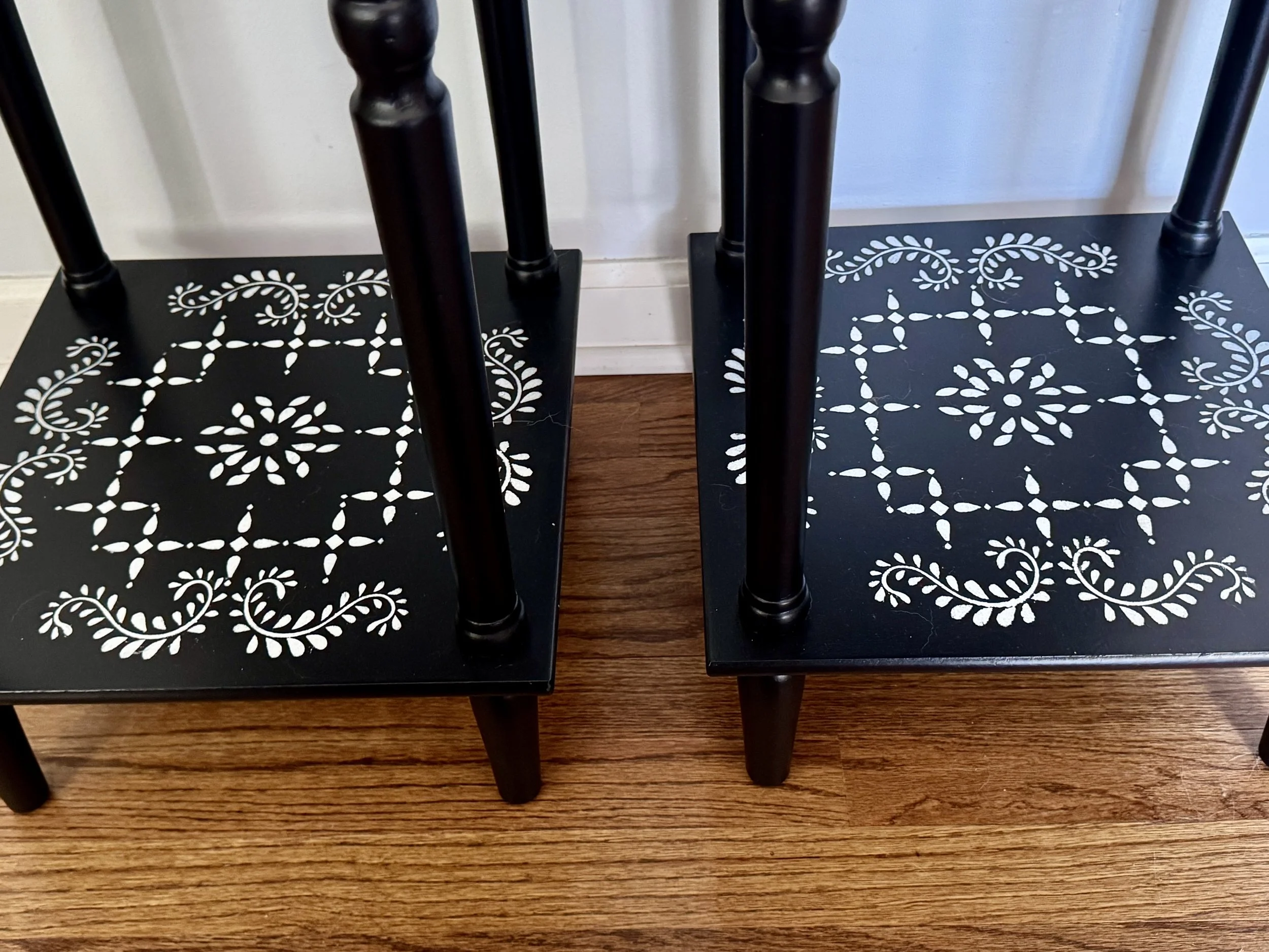 Two black tables with white decorative patterns on top of a wooden floor.