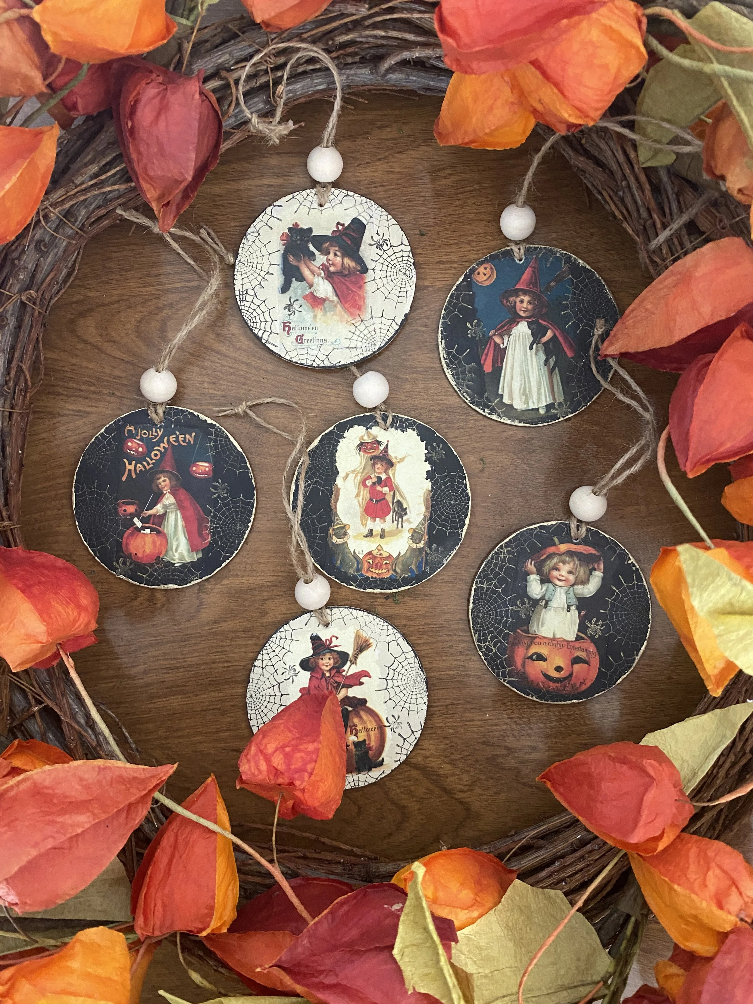 Decorative Halloween wreath with orange and yellow leaves and vintage-style Halloween-themed circular cutouts, including a girl in a witch costume, a girl with a witch hat, a girl in a white dress with a pointy hat, and a smiling pumpkin, hanging on 