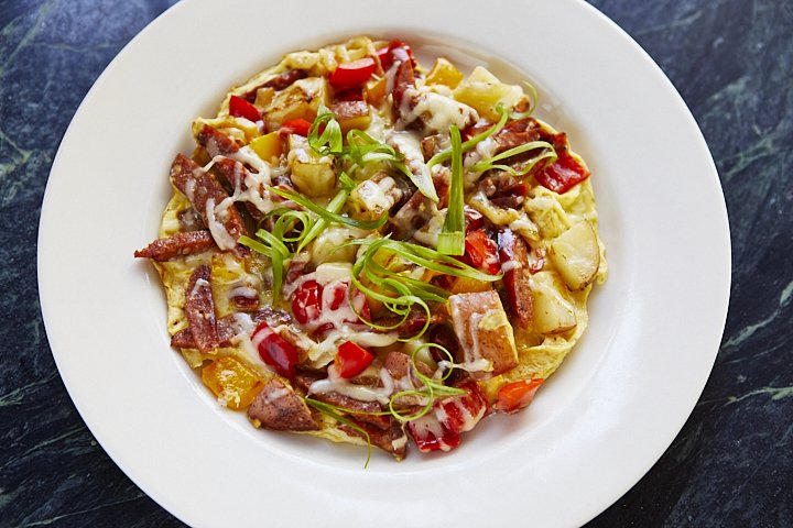 A plate of breakfast nachos with cheese, bacon, potatoes, tomatoes, and green onions.