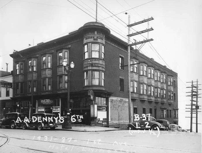 Black and white photo of a corner hotel building with multiple cars parked in front, street signs, and utility poles.