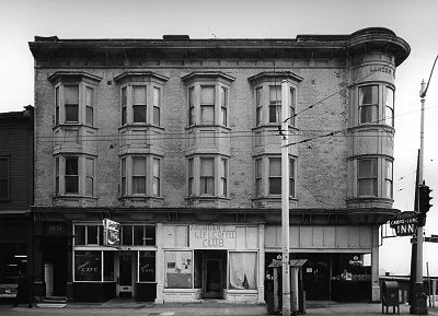 Black and white photo of a three-story building with bay windows, a coffee club, a cafe, and an inn on the ground floor.