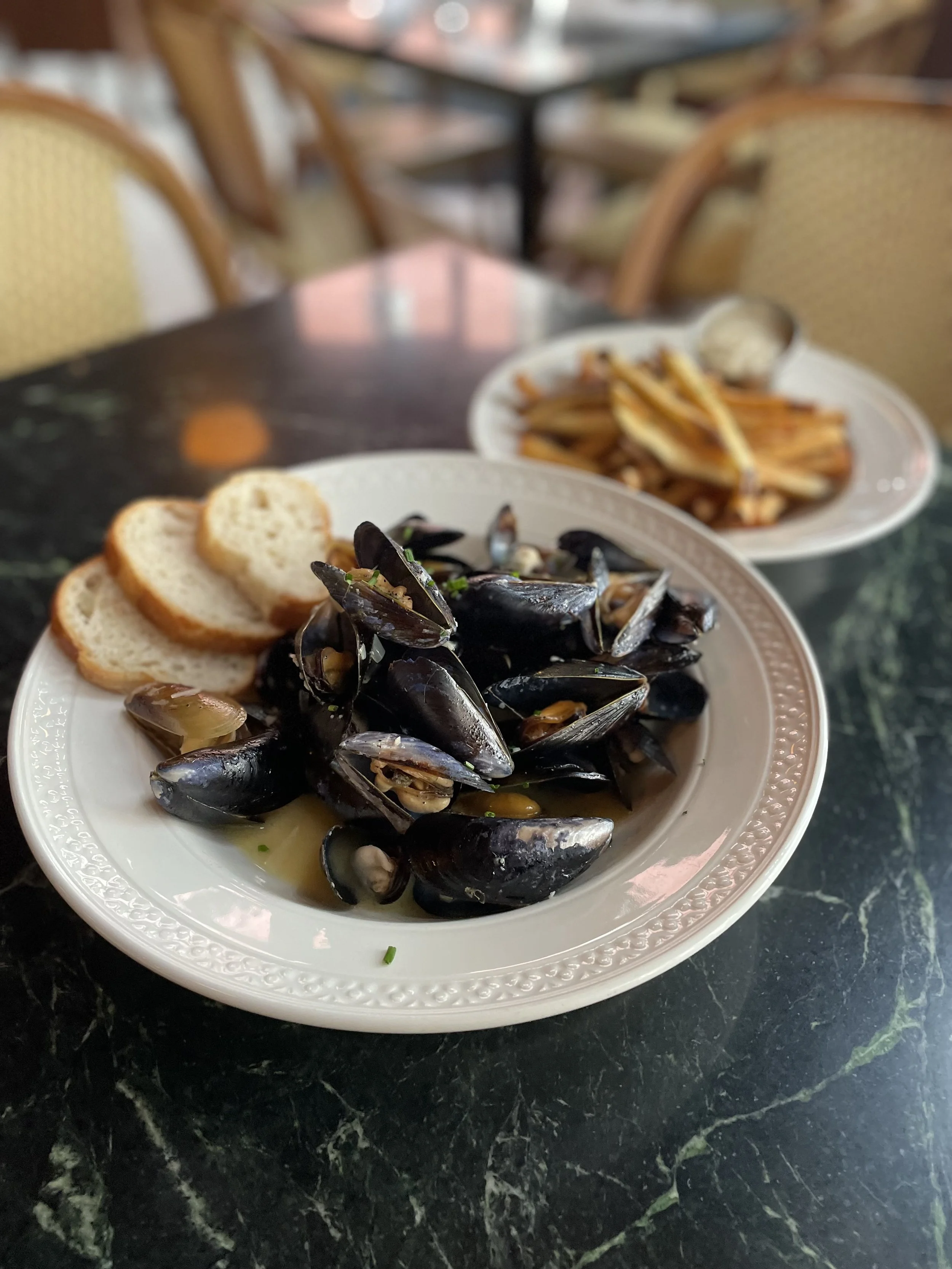 A plate of cooked mussels with slices of bread on the side, on a dark marble table at a restaurant.
