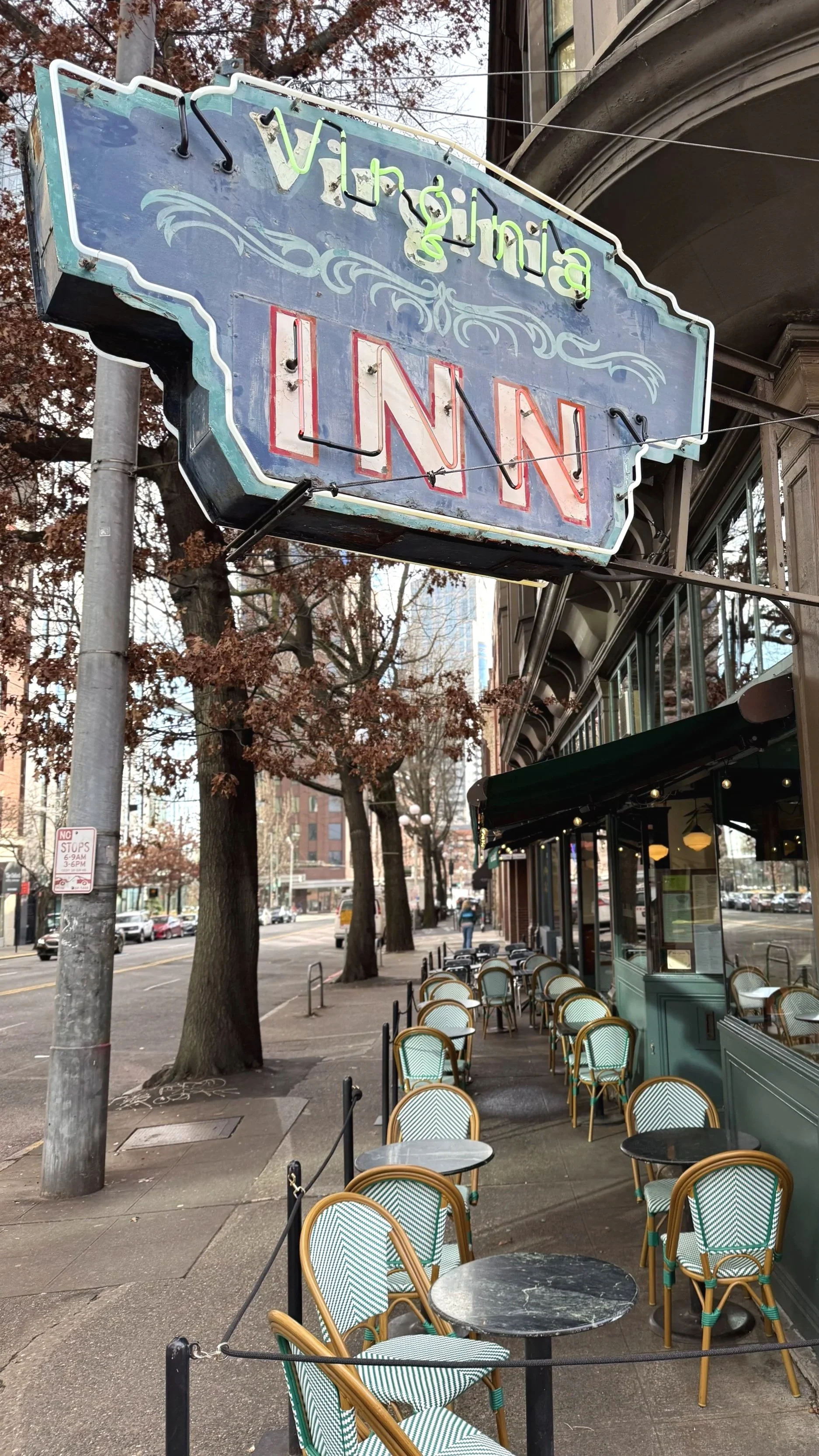 Outdoor cafe with chairs and tables along a city sidewalk, with a vintage neon sign for Virginia Inn hanging above.