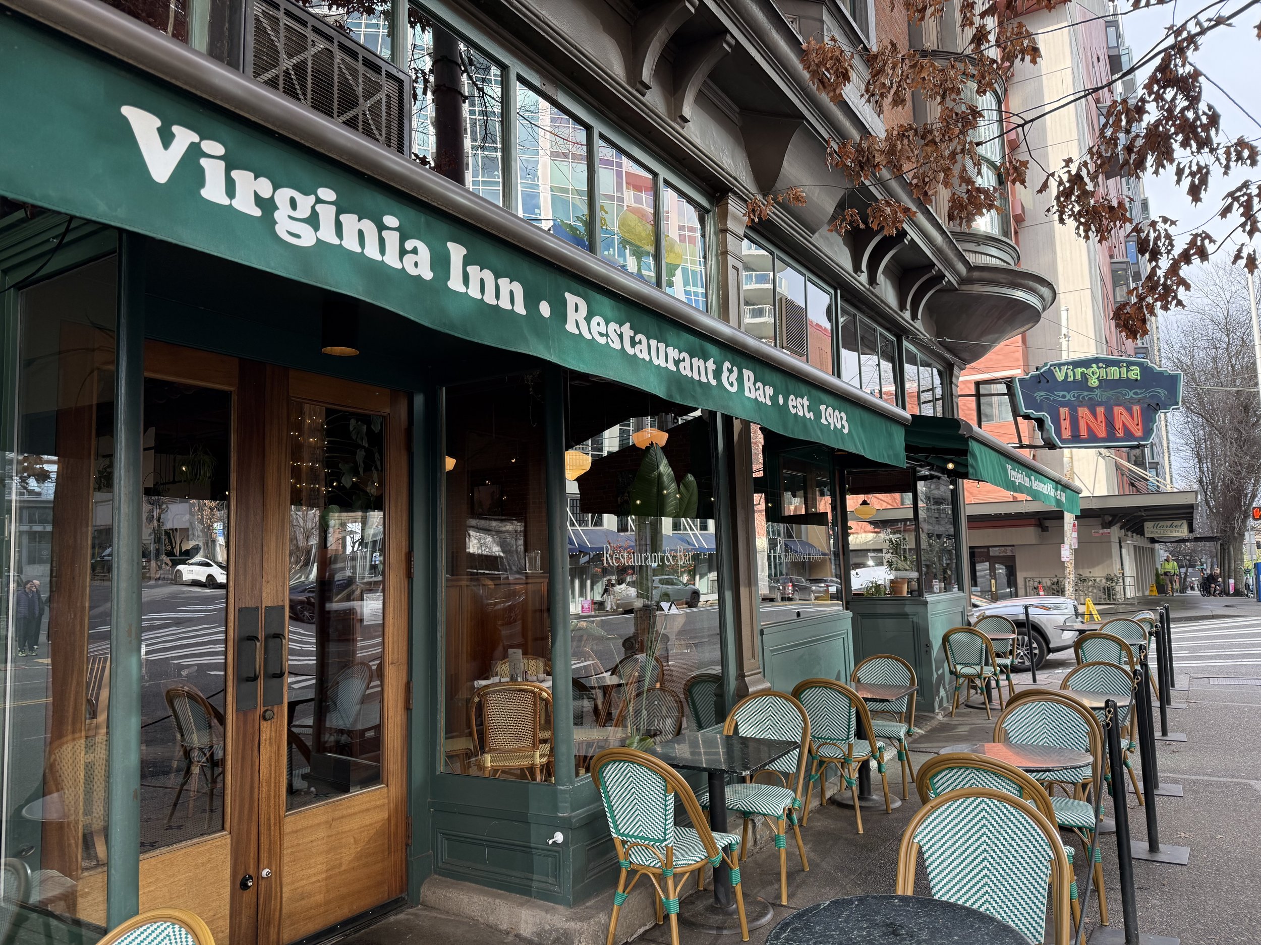Exterior view of Virginia Inn, a restaurant and bar established in 1903, with outdoor seating and green awning, located on a city street.