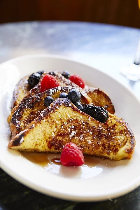 French toast topped with fresh berries, powdered sugar, and syrup on a white plate.