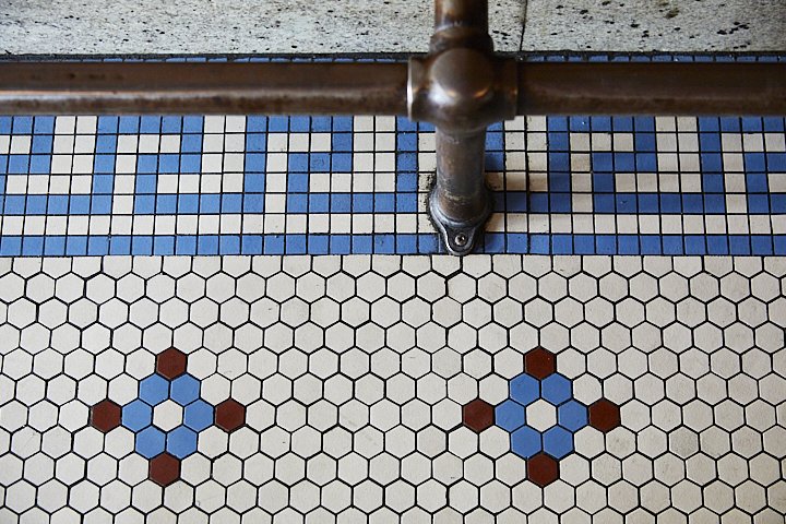 Patterned tile floor with hexagonal tiles and a decorative border, partially obscured by a pipe and railing.