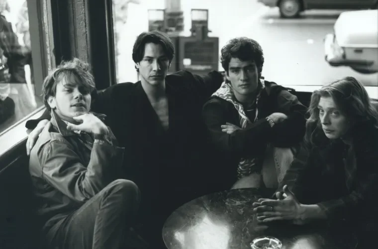 Four young people sitting around a table in a diner, two men and two women, with a window and street scene in the background.