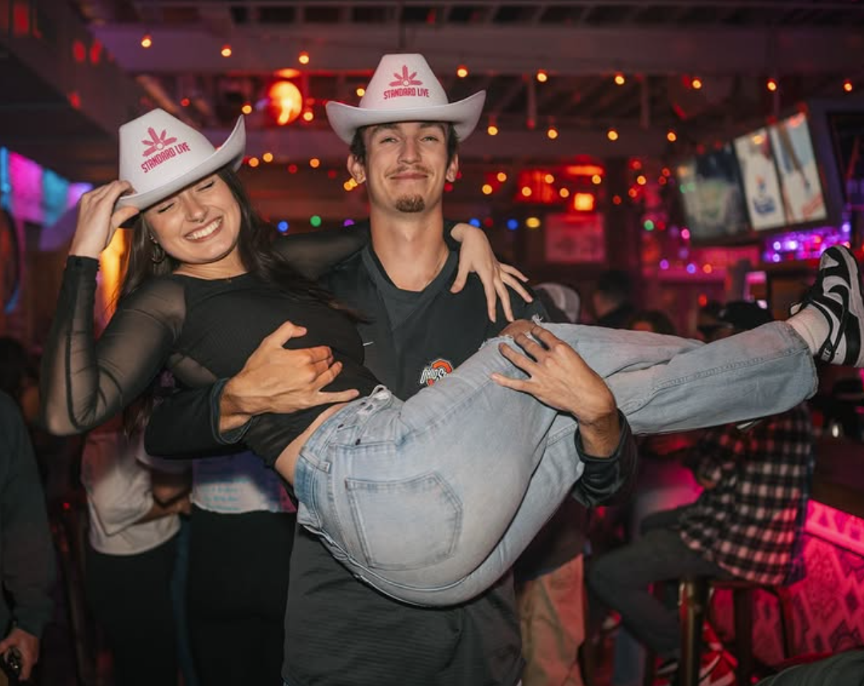 Couple wearing white Standard Live branded cowboy hats during a night out at a country bar.
