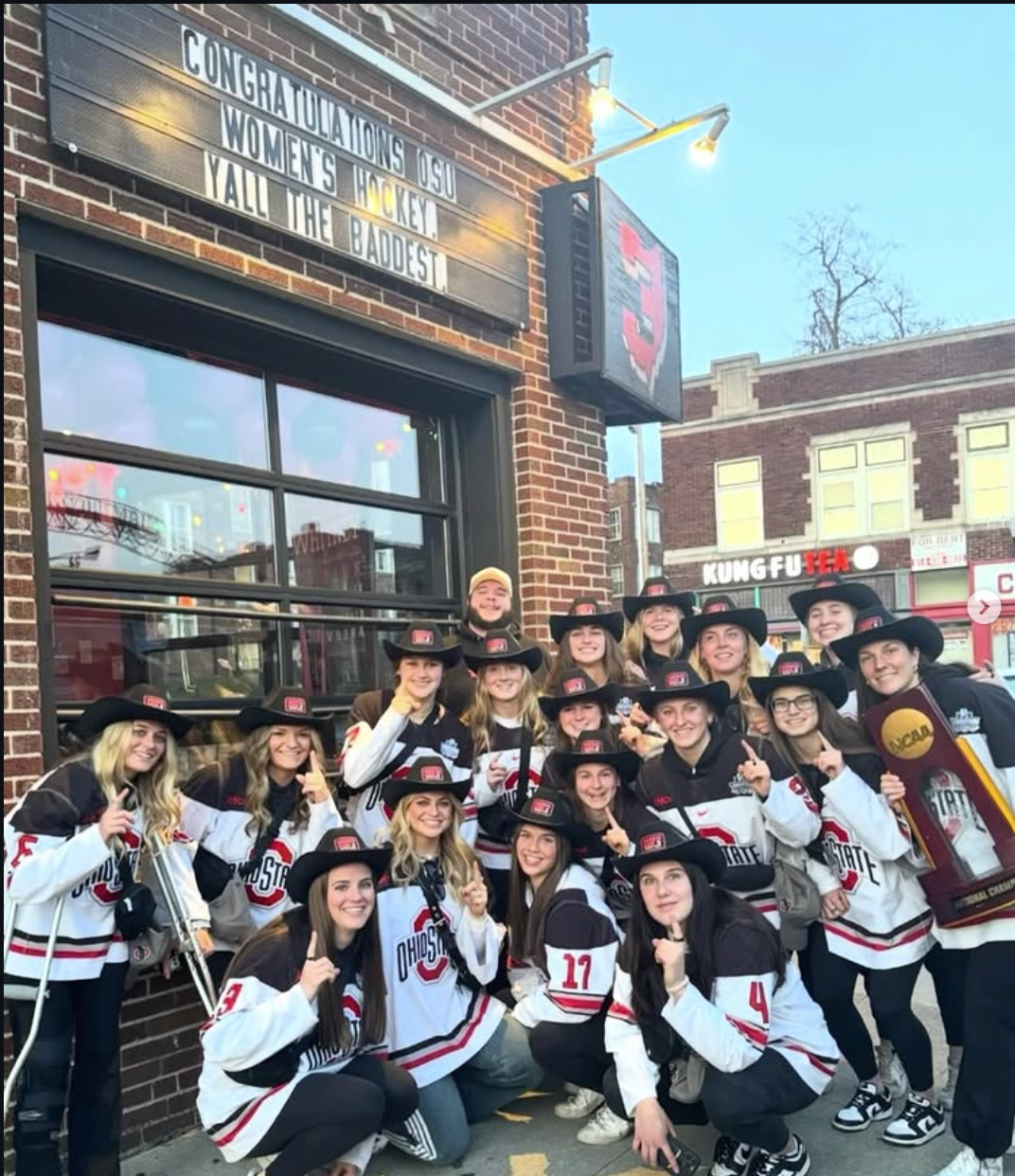 Ohio State women’s hockey group wearing matching black promotional cowboy hats outside a bar.