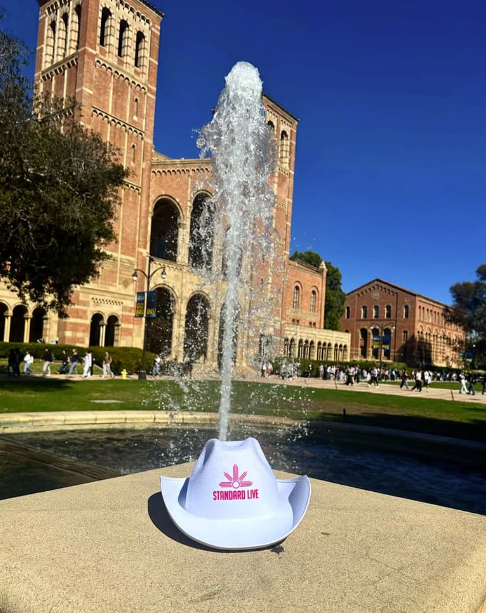 White Standard Live branded cowboy hat displayed by a fountain in front of Royce Hall on the UCLA campus.