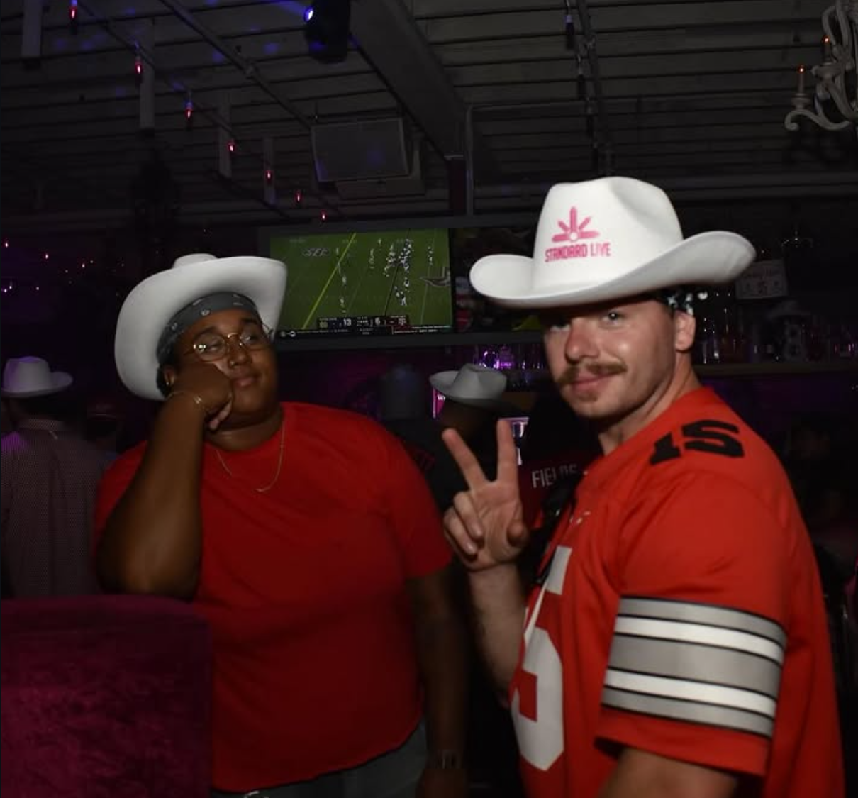 Two bar guests wearing promotional cowboy hats during a football game at a nightlife venue.