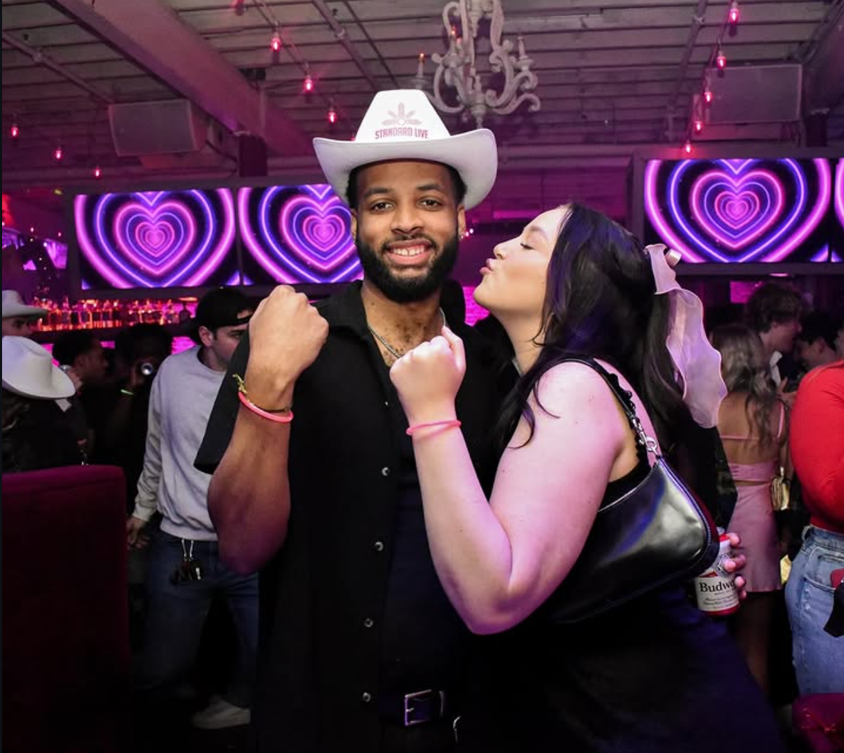 Bar guests posing together with a white Standard Live promotional cowboy hat in a nightlife setting.