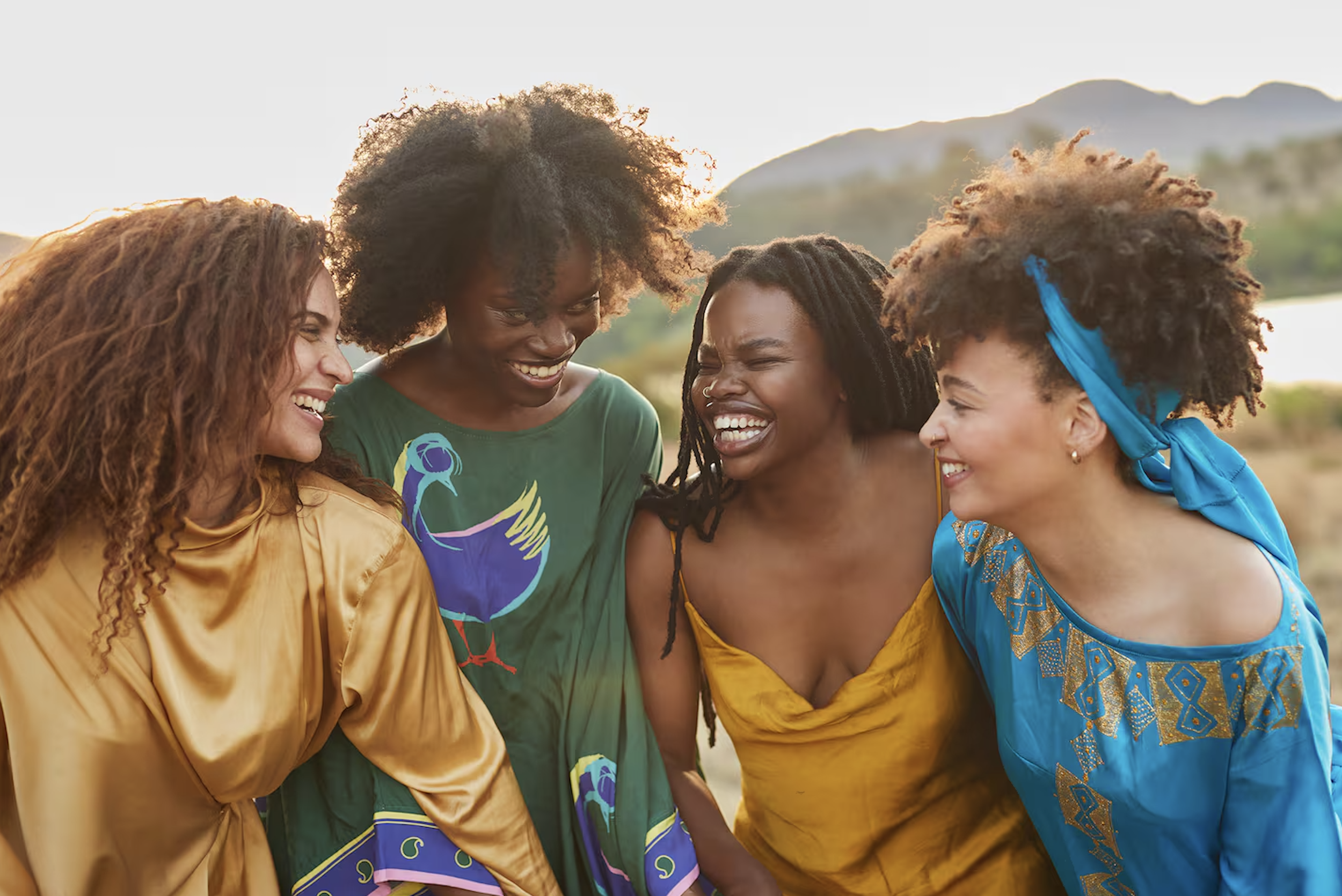 Quatre femmes africaines souriantes rassemblées dans un paysage naturel avec des montagnes en arrière-plan.