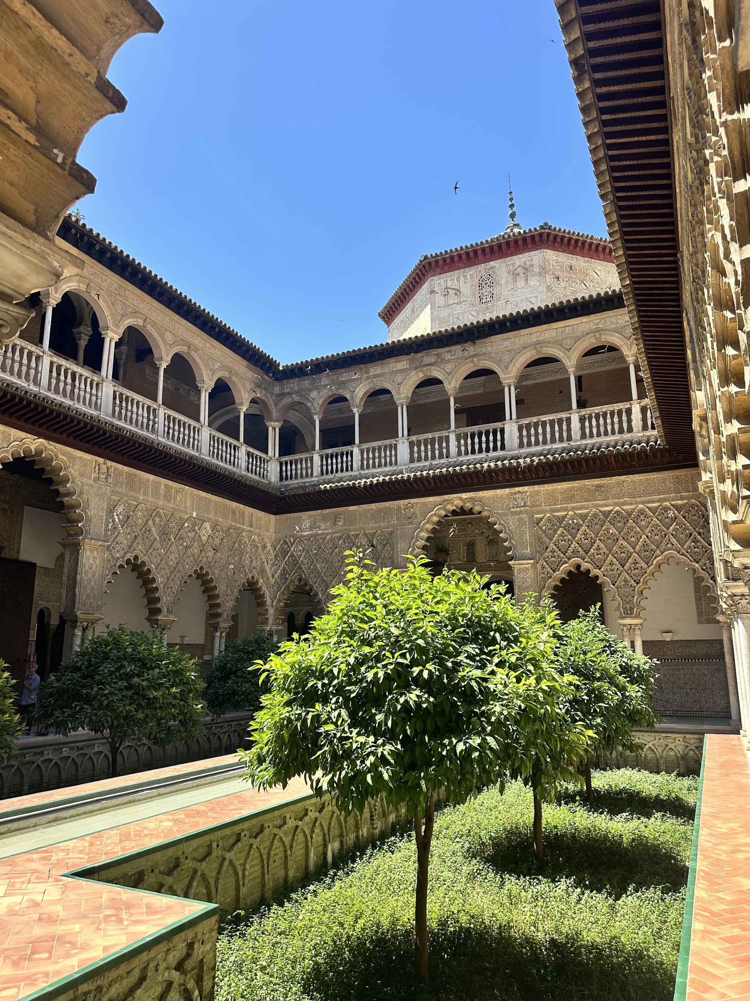 Royal Alcázar courtyard in Seville, Spain, featuring historic architecture, lush gardens, and natural light that create a sense of calm, beauty, and connection.