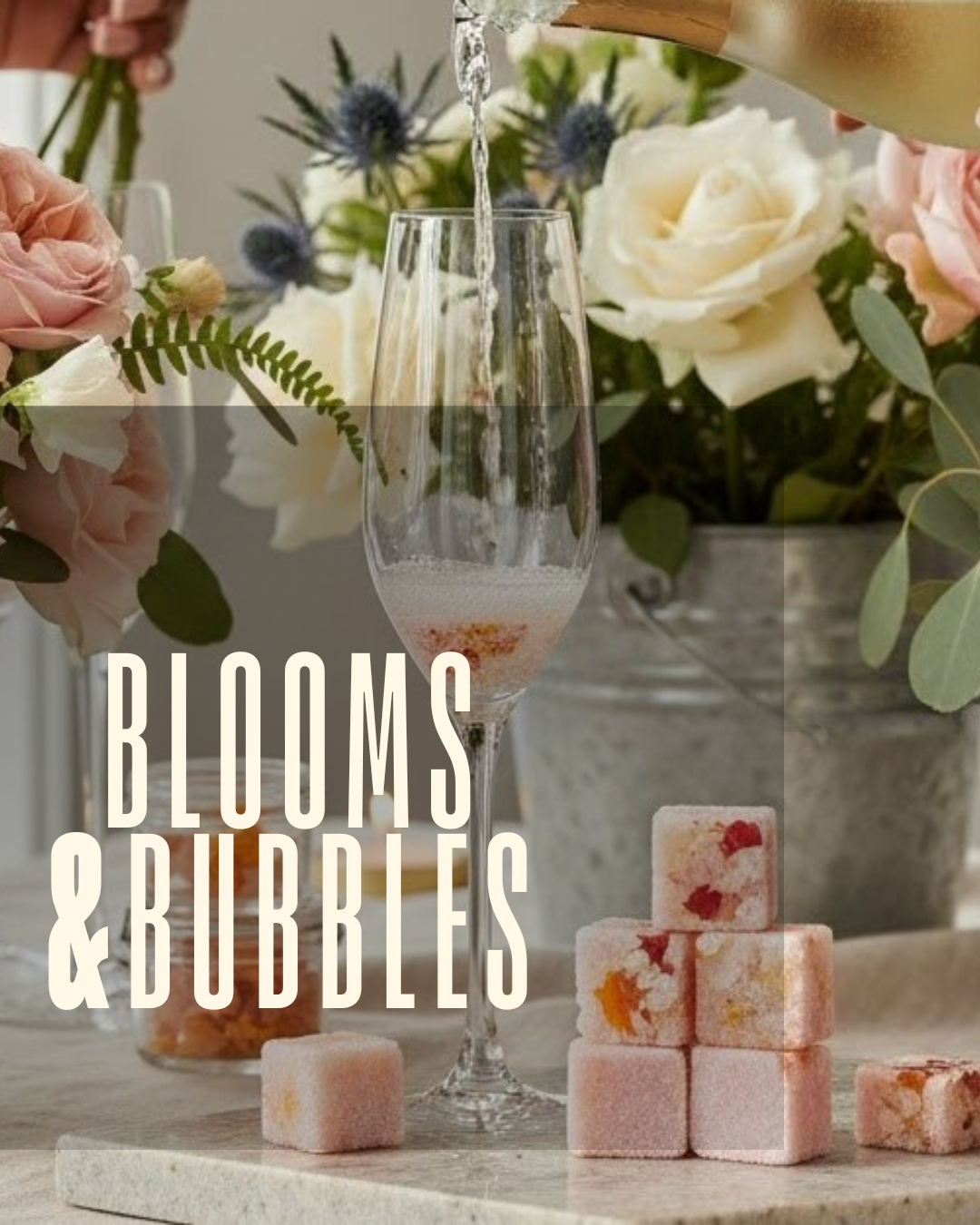 A champagne flute being filled with sparkling wine, surrounded by a floral arrangement with white and pink roses, purple thistles, and green leaves. Several pink and orange floral ice cubes are on the table in front of the glass, with a background of flowers in a vase.