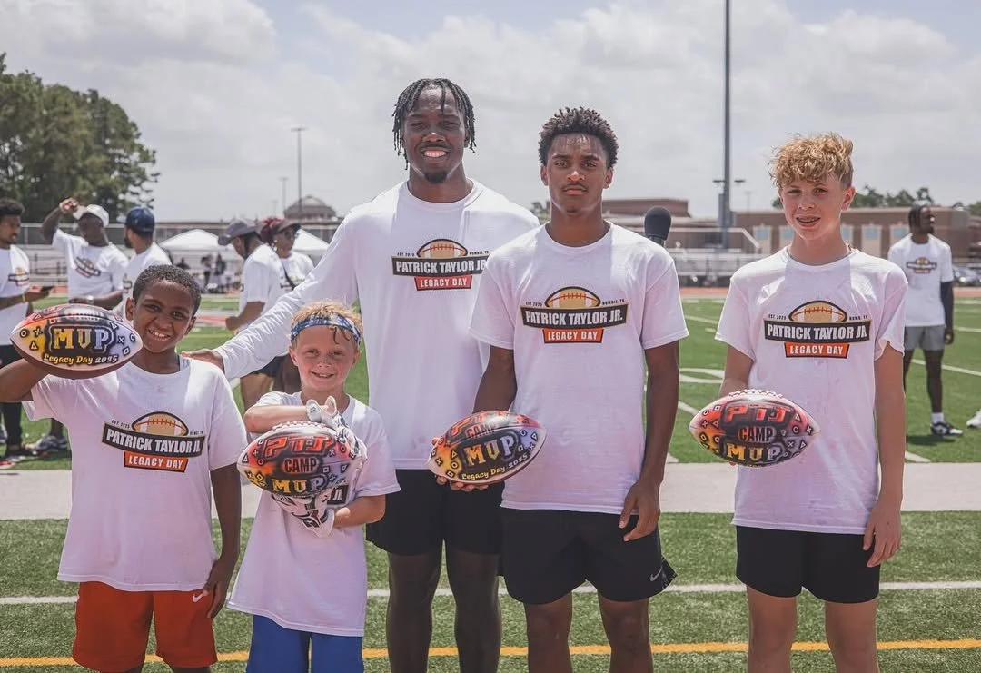 Group of five young boys and one adult standing on a football field, holding footballs, during a sports event called Patrick Taylor Jr. Legacy Day 2019.