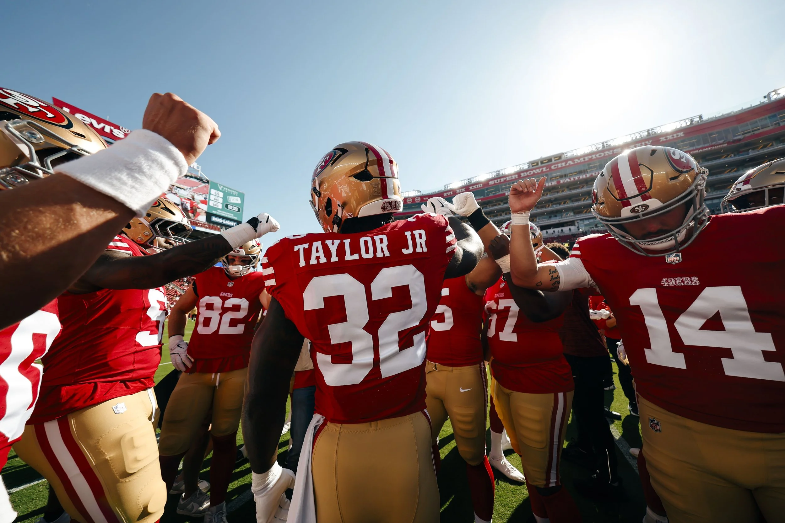 San Francisco 49ers football team players wearing red and gold uniforms on the field during a game, with some players raising their fists or arms in celebration.