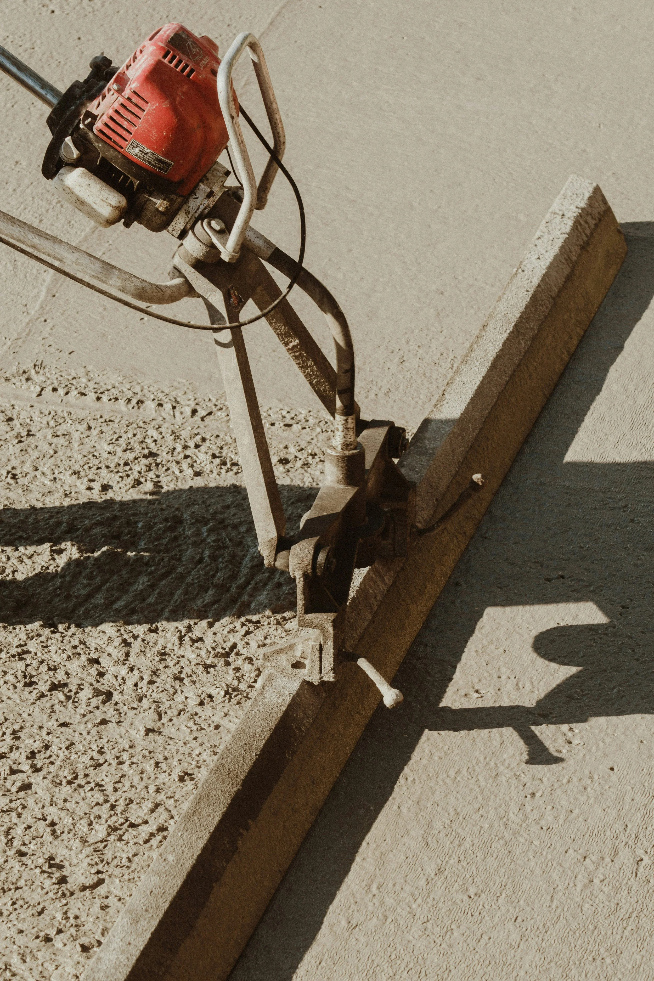 A concrete finishing machine smoothing a freshly poured concrete surface, casting a shadow.
