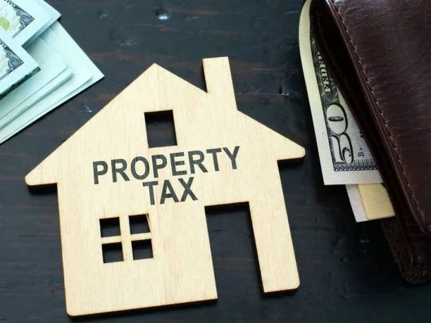 Image of a wooden cutout of a house with "Property Tax" burned into it next to a wallet and cash.