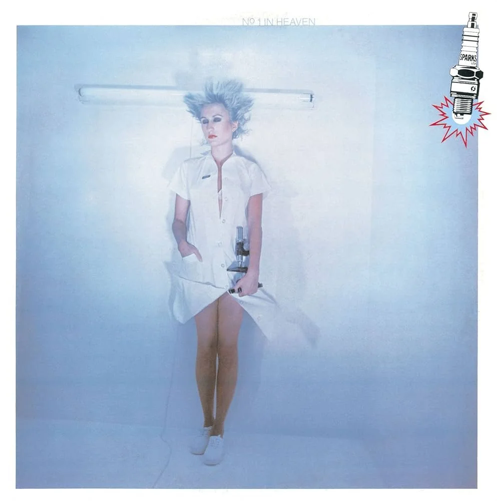 A woman in a white nurse outfit holding a microscope, standing against a plain light background, with a spotlight overhead, and a large spark plug illustration in the upper right corner.