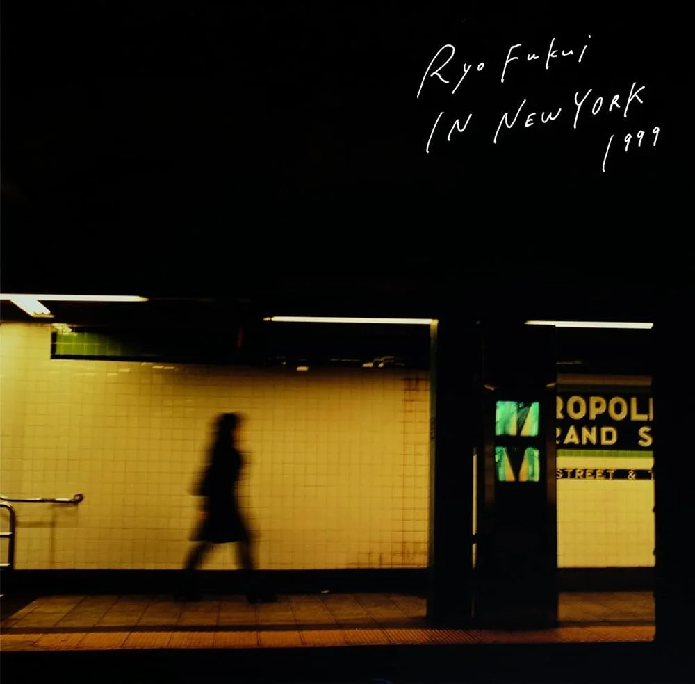 A person walking through a subway station with yellow tiled walls, dark ceiling, and overhead lights. Handwritten text in the top right corner reads 'Ryo Fukui in New York 1999'.