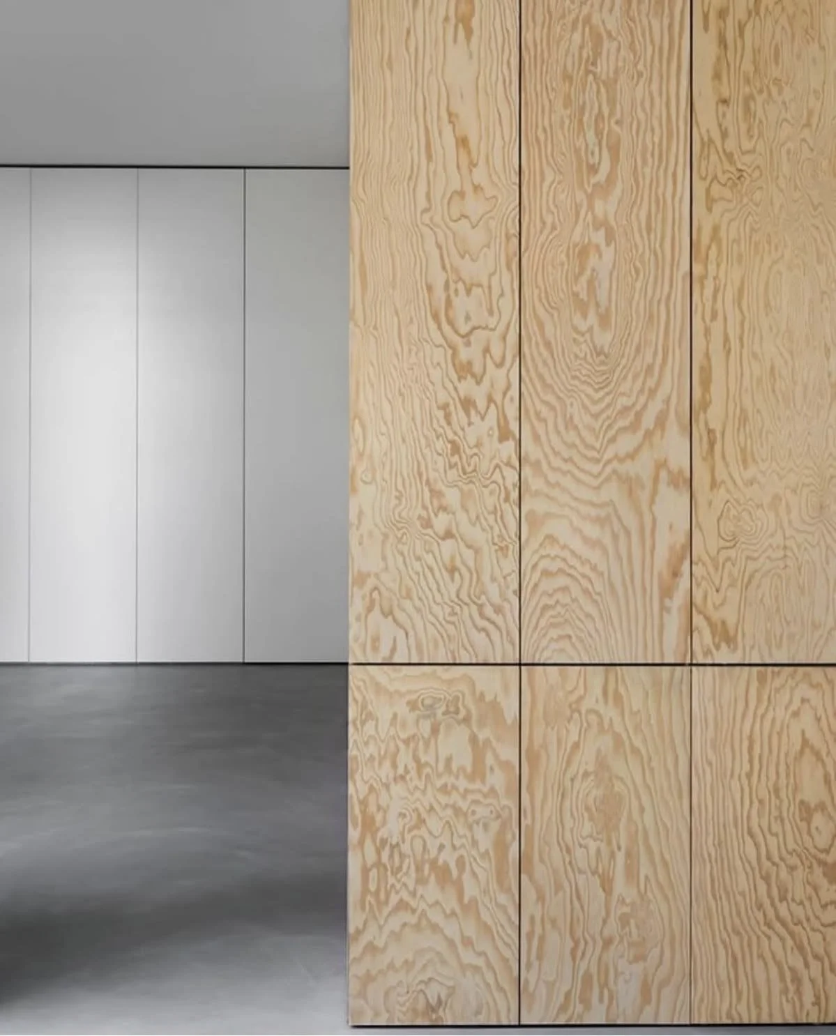 Interior view of a modern space with a wooden panel wall on the right, and a gray wall on the left, with a polished concrete floor.