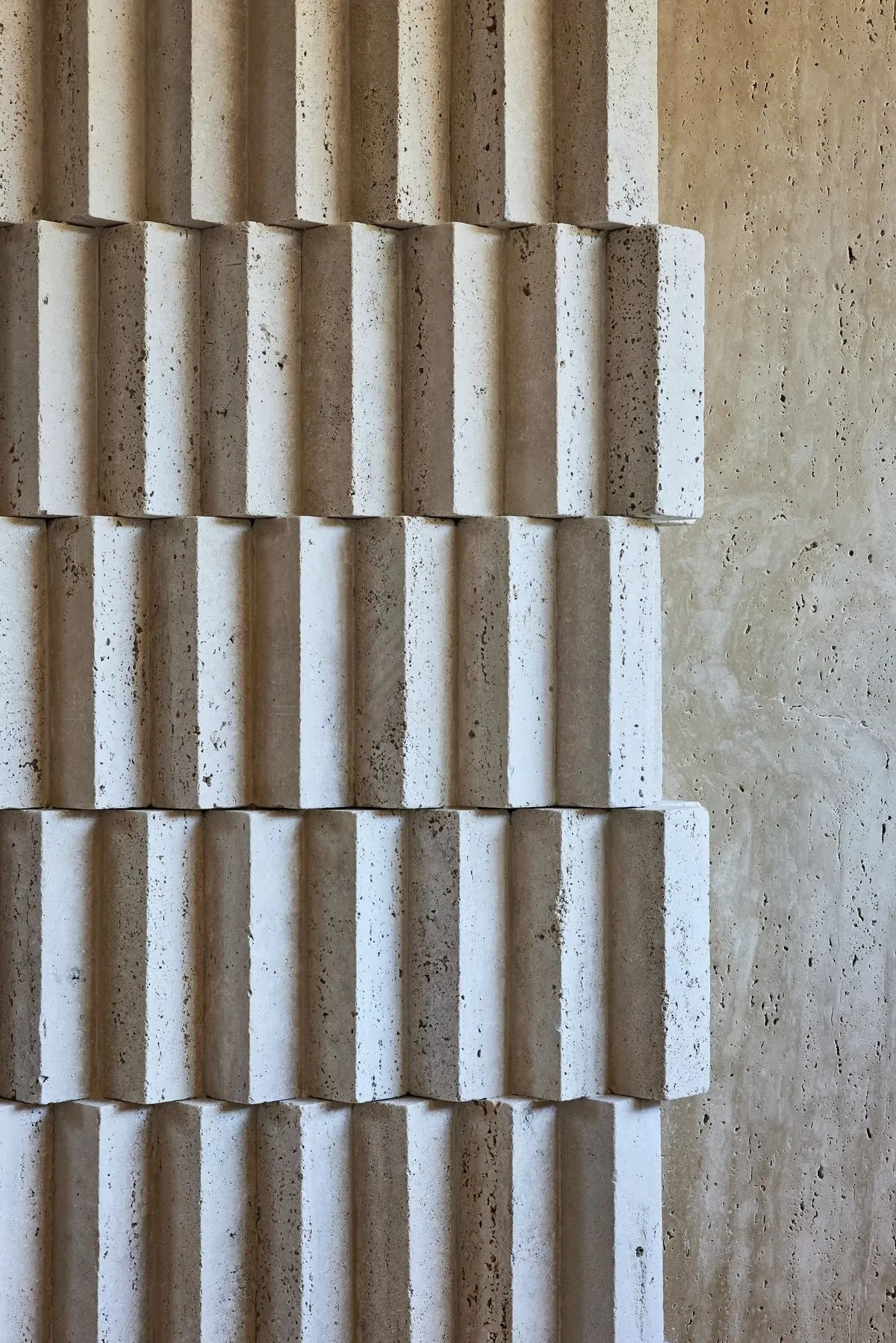 Close-up of a wall with decorative three-dimensional textured tiles arranged in a vertical pattern, beige and cream-colored.