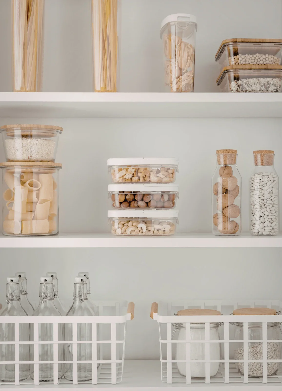 Organized pantry with glass jars, plastic containers, and baskets filled with pasta, rice, nuts, and grains.