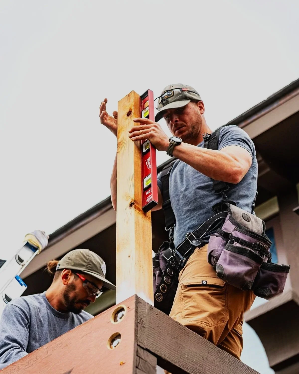 Two construction workers leveling a wooden post on a house roof with a spirit level tool.