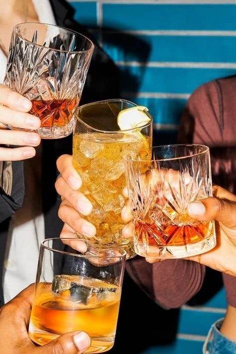 Four people holding different cocktails in glasses, making a toast, with a blue background.