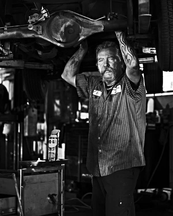 A mechanic working underneath a lifted vehicle in a garage, with tools and equipment around.
