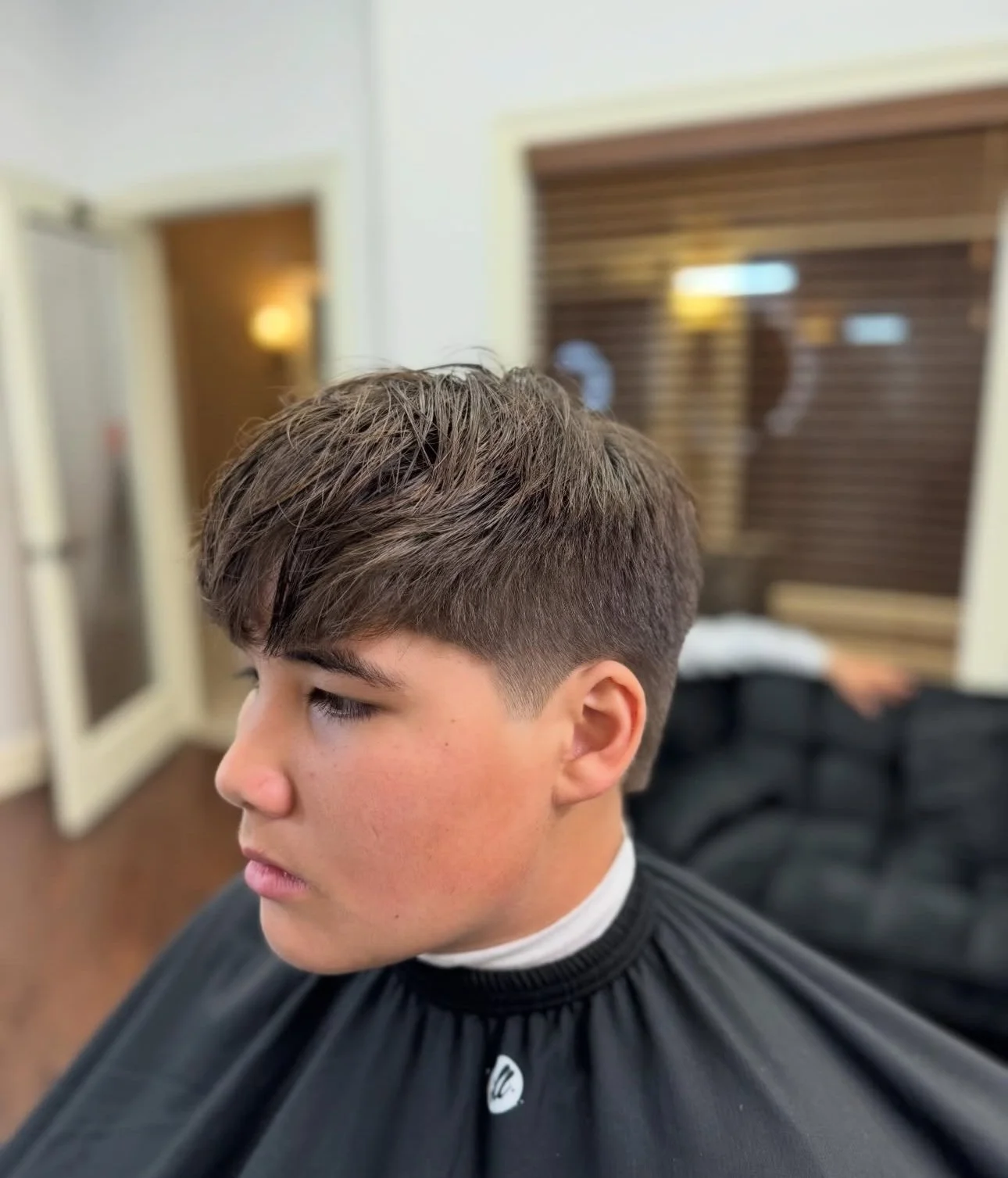 Close-up of a young man's side profile with a fresh haircut, sitting in a barber shop.