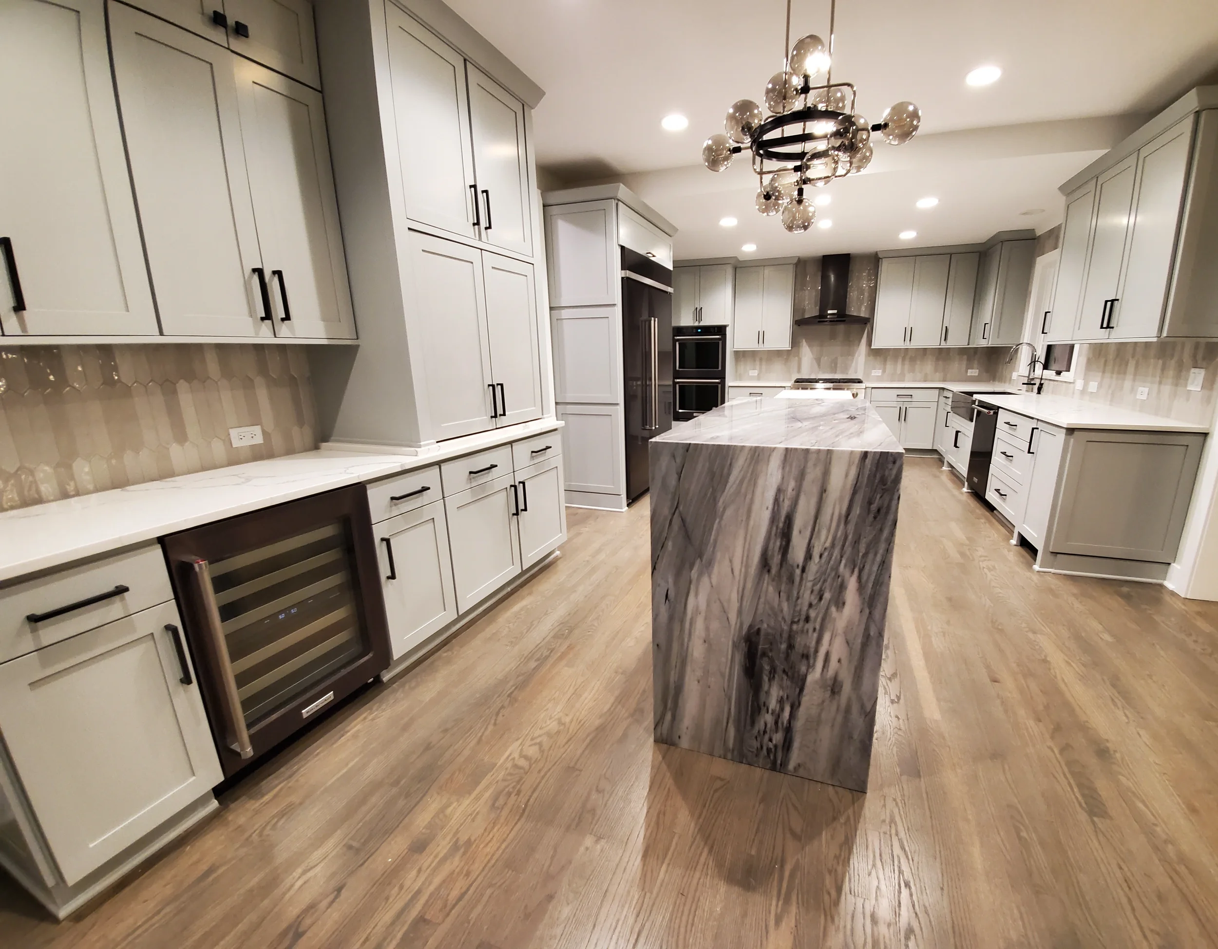 A spacious luxury kitchen in a Barrington Hills estate featuring newly refinished white cabinets, a large dark wood island with a marble countertop, and modern lighting fixtures by Kora Pro Painting.