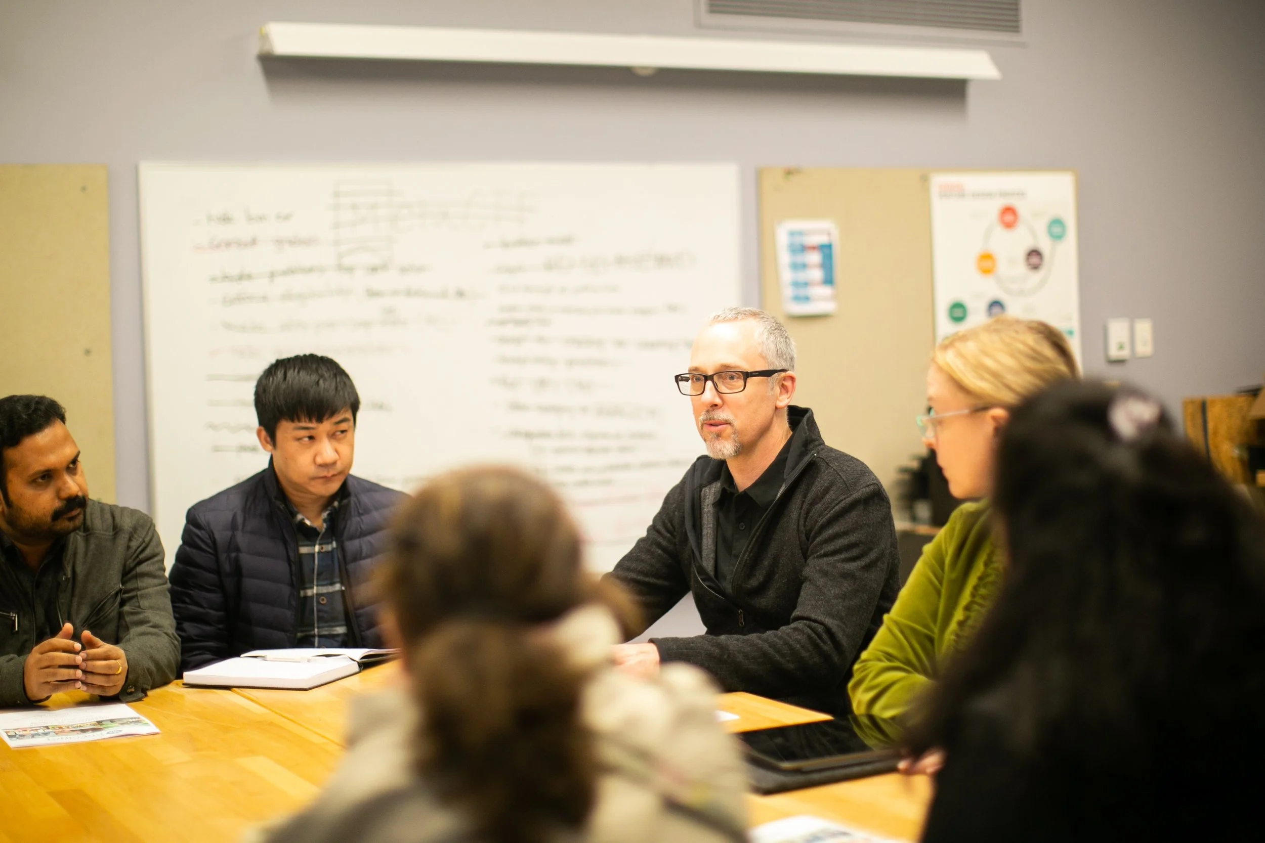 People sit around a table talking in an office with a whiteboard in the background