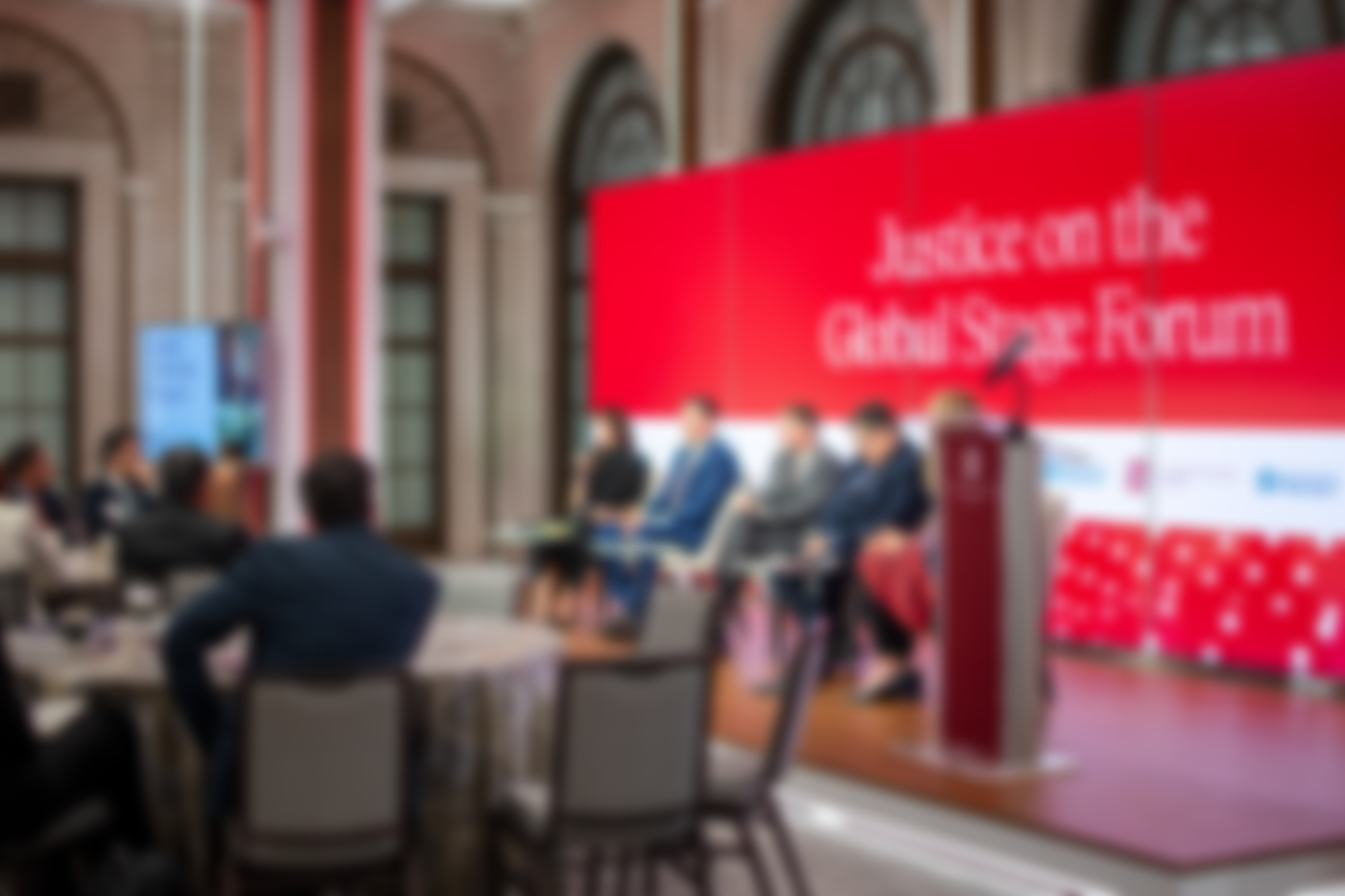 Blurry photo of a conference or panel discussion with several people sitting at tables.