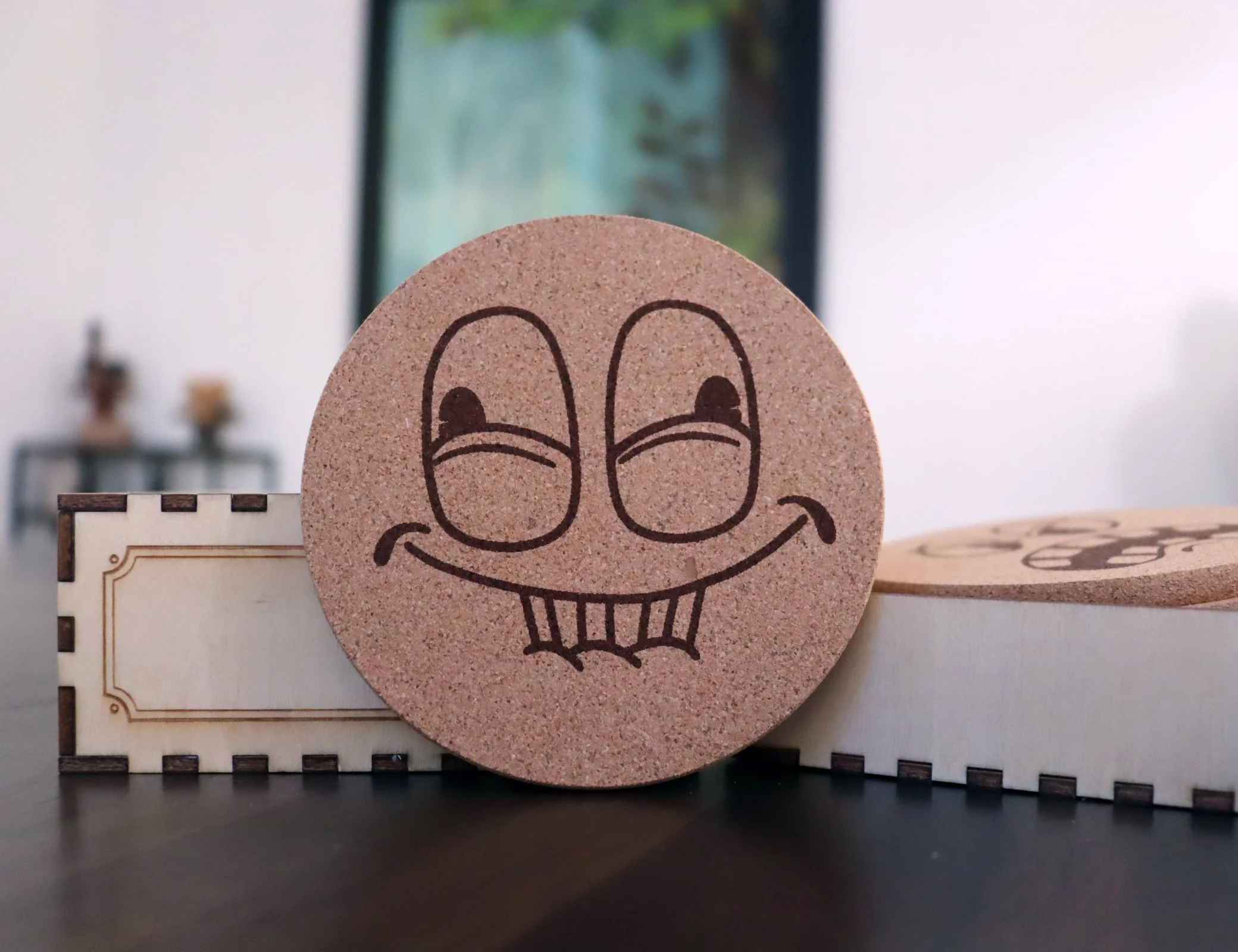 Holdin_A_Hoot cork coaster with a sly cartoon face holding back laughter