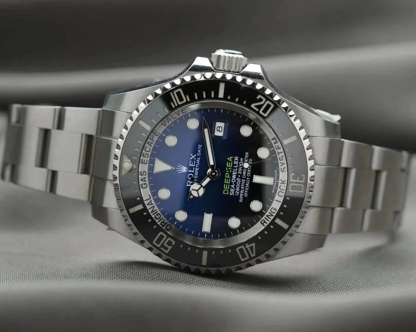 Close-up of a Rolex Deepsea Sea-Dweller watch with a black bezel and blue dial, featuring white markers, a date window at 3 o'clock, and a stainless steel bracelet.