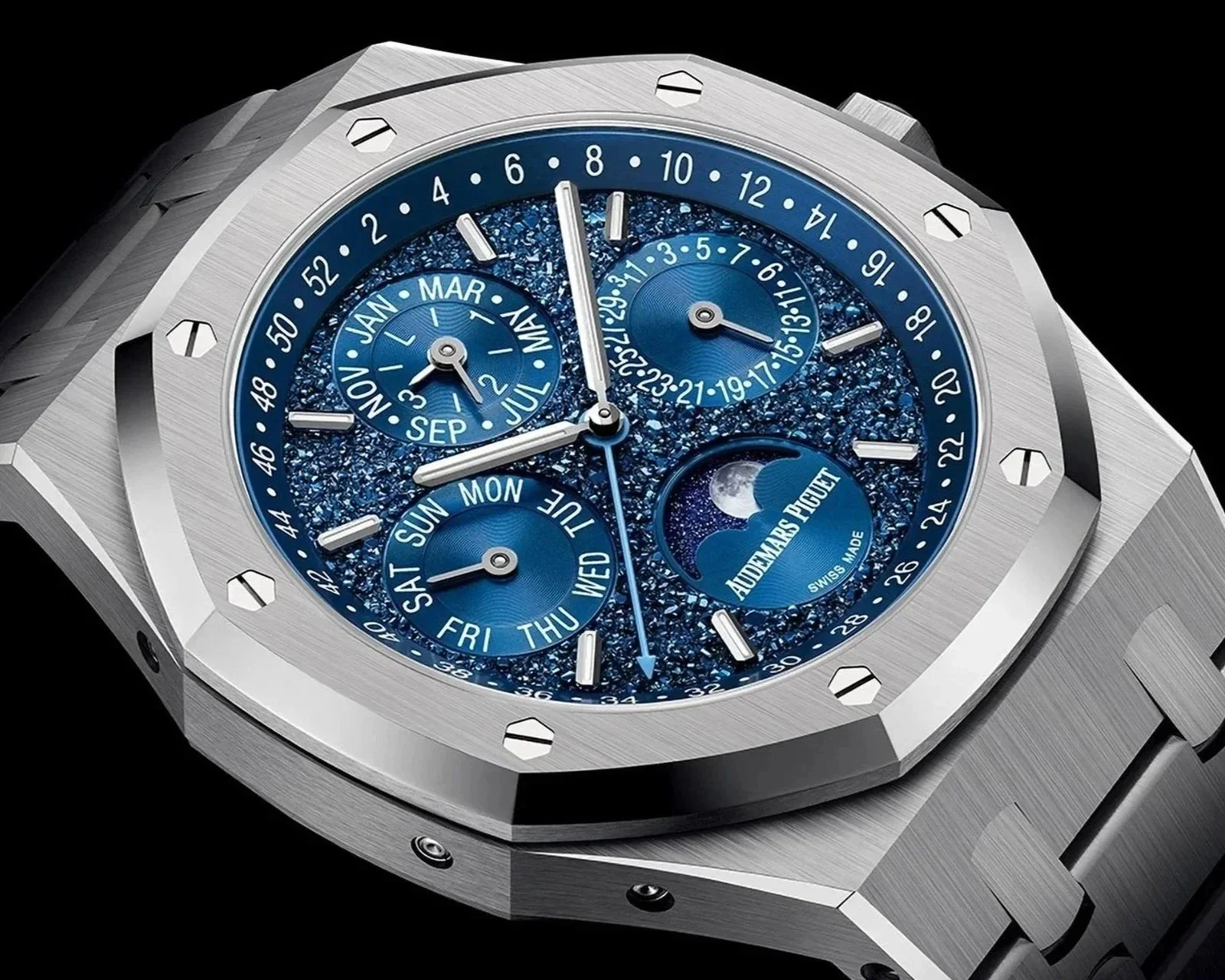 Close-up of a luxury Audemars Piguet watch with a blue textured dial showing day, date, month, moon phase, and time.